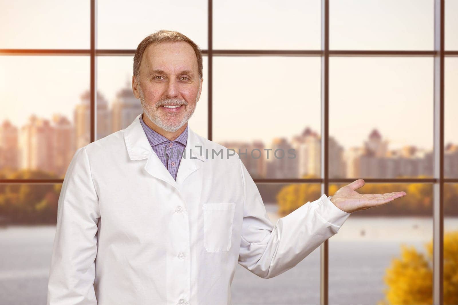 Happy smiling male senior doctor showing a copy space. by super_picture