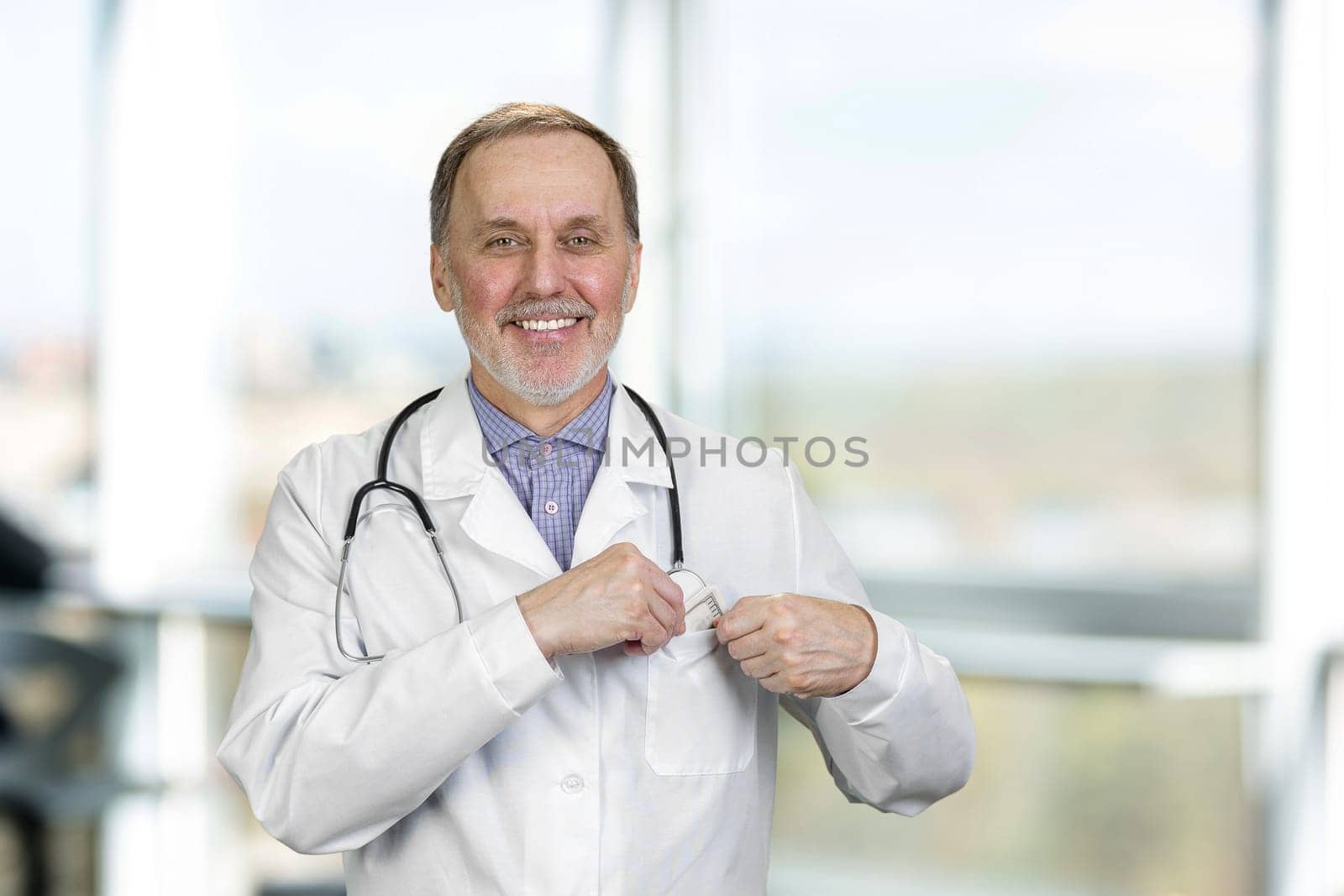 Portrait of happy senior male doctor puts money in his pocket. by super_picture