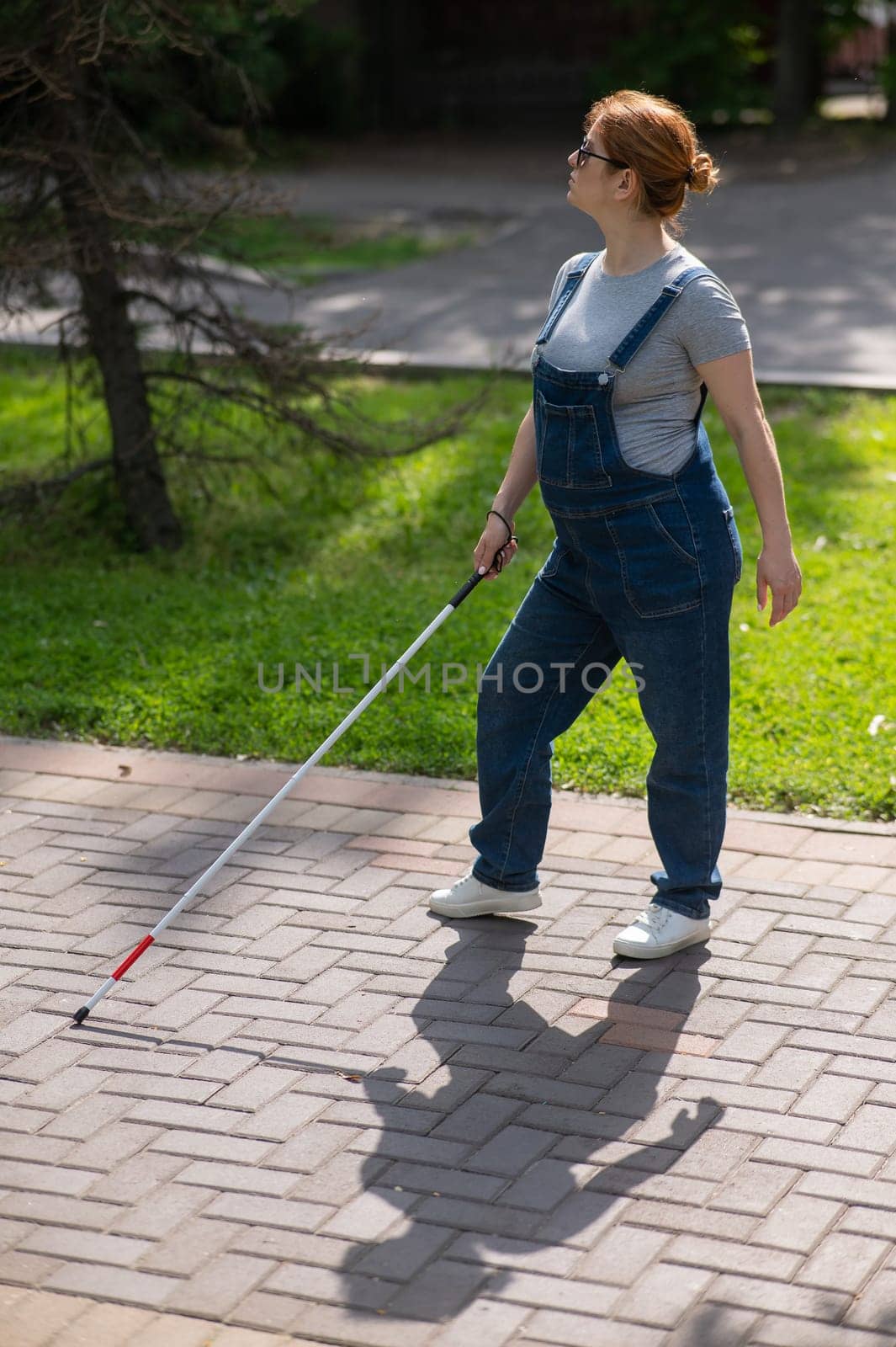 Blind pregnant woman walking in the park with a cane