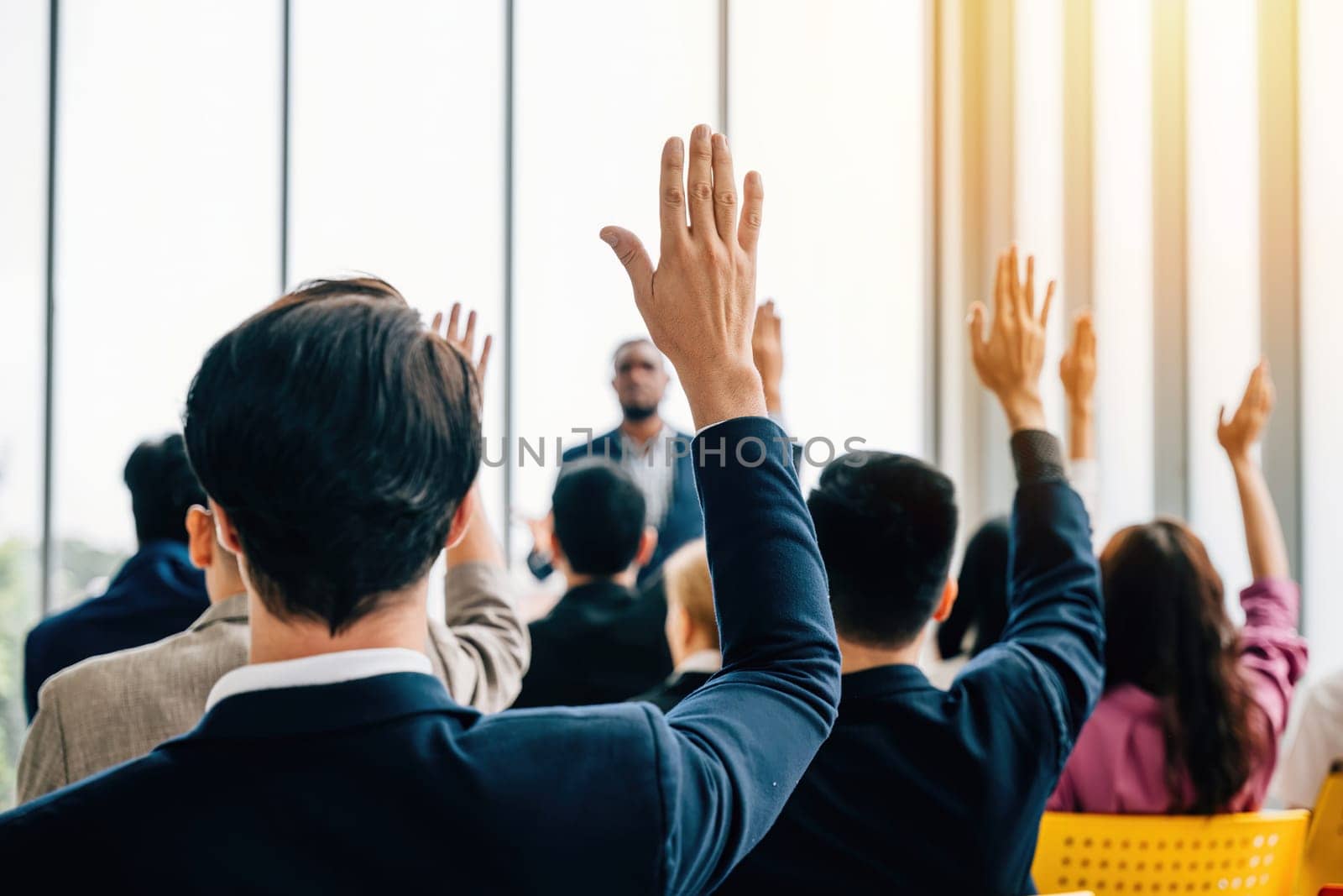 In the boardroom business professionals meet for a strategy session. The meeting and seminar feature raised hands as questions are posed by colleagues and employees.