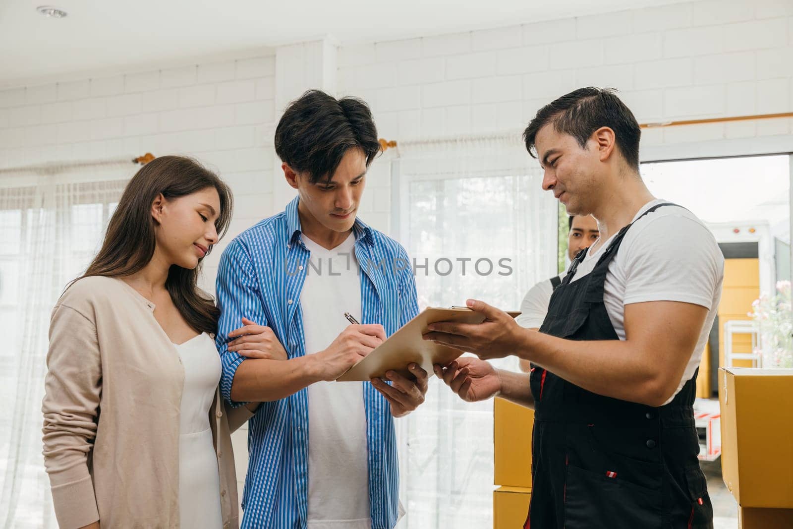 Before signing moving documents family inspects checklist boxes. Worker holds a box. Professional movers ensure reliable relocation service. Efficient teamwork and home relocation shown. Movind Day