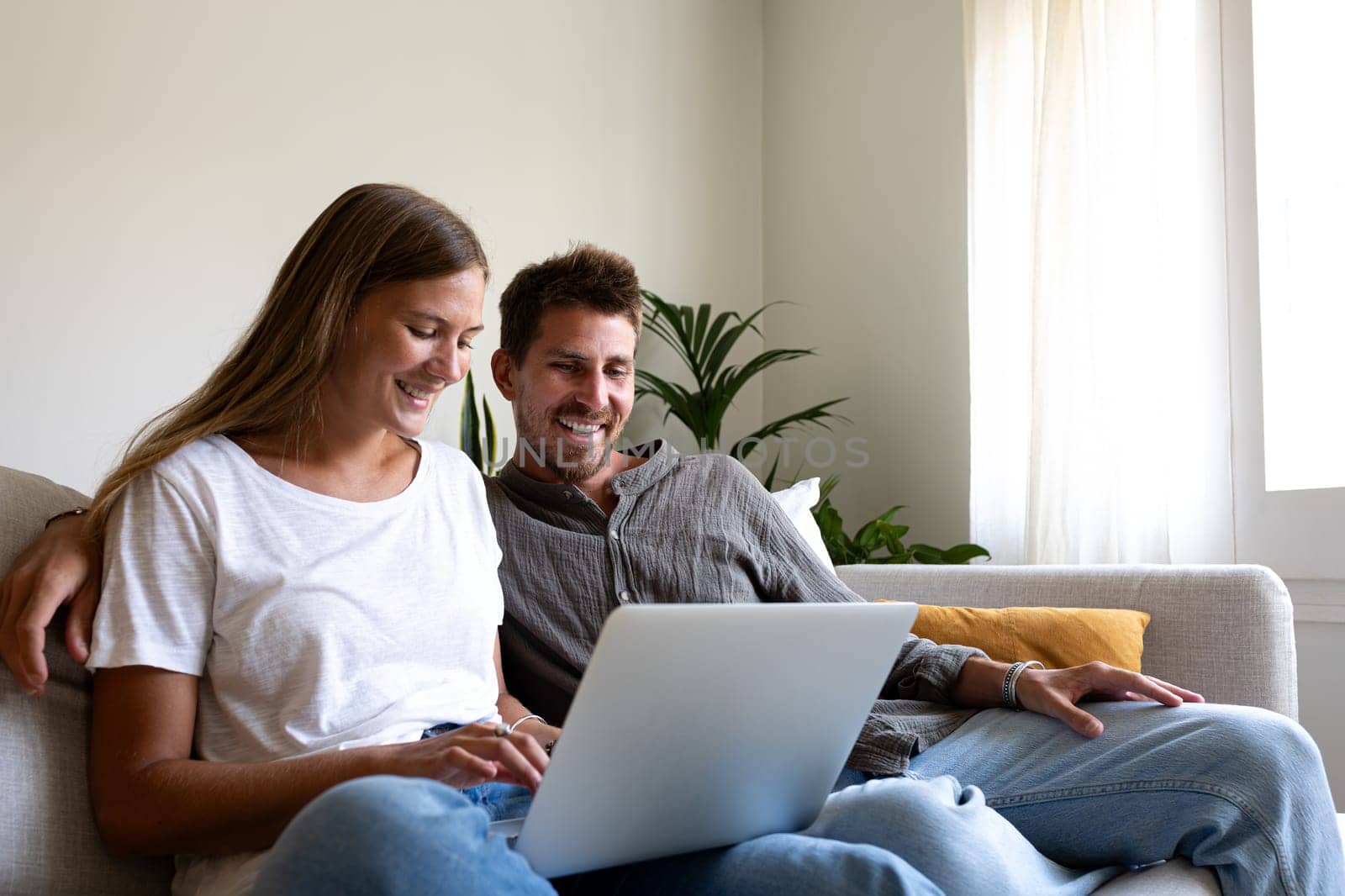 Happy young couple using laptop relaxing sitting on the sofa ordering online. Copy space. by Hoverstock