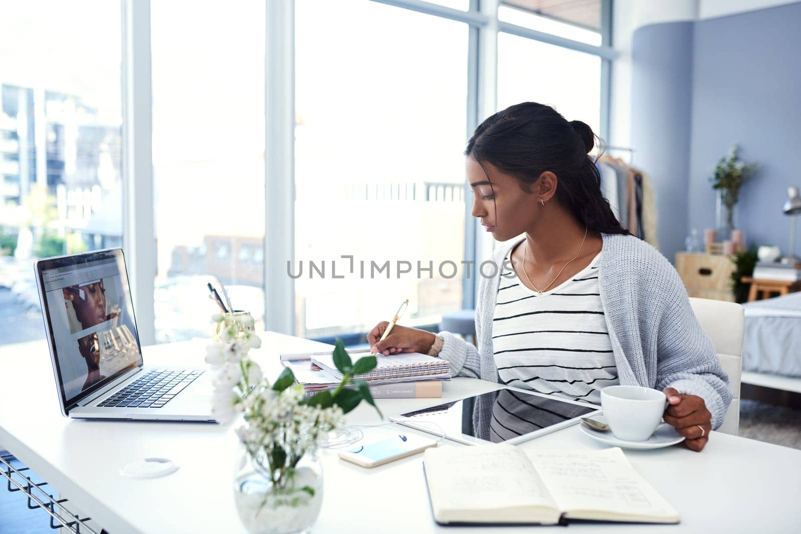 Girl, laptop and student writing in home, study and learning workspace in bedroom for online elearning. Notebook, tech for internet search or social media, coffee and serious and tablet for notes by YuriArcurs