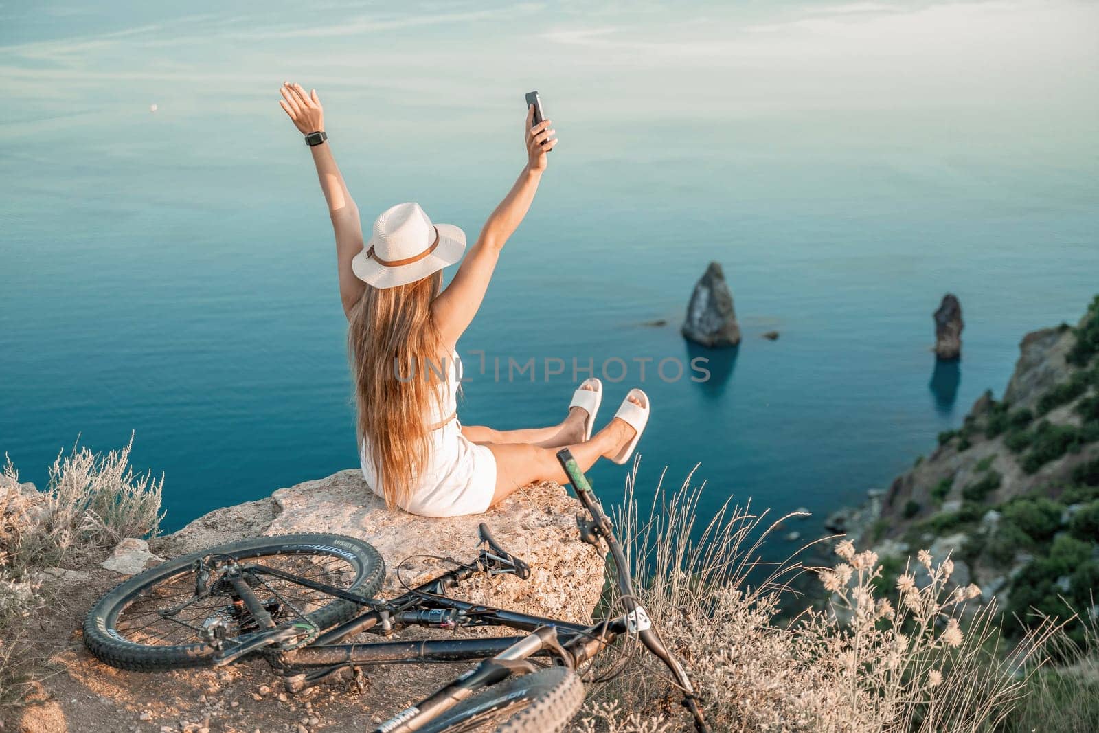 A woman cyclist on a mountain bike looking at the landscape of mountains and sea. Adventure travel on bike