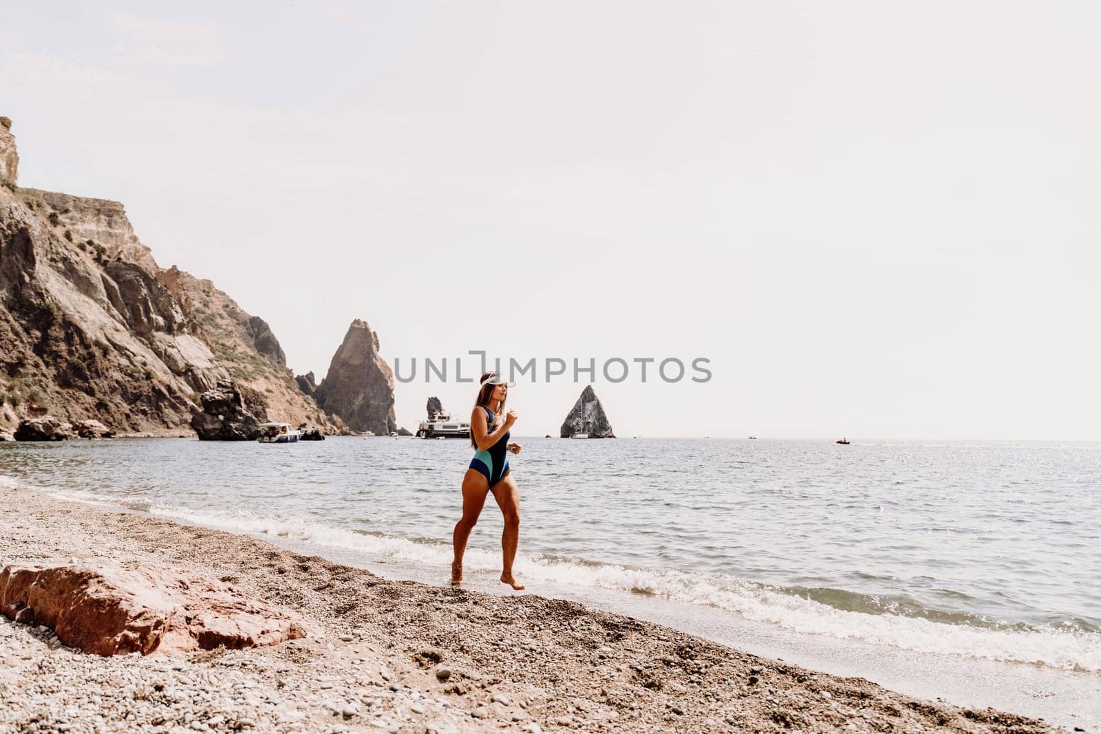 Woman beach vacation photo. A happy tourist in a blue bikini enjoying the scenic view of the sea and volcanic mountains while taking pictures to capture the memories of her travel adventure