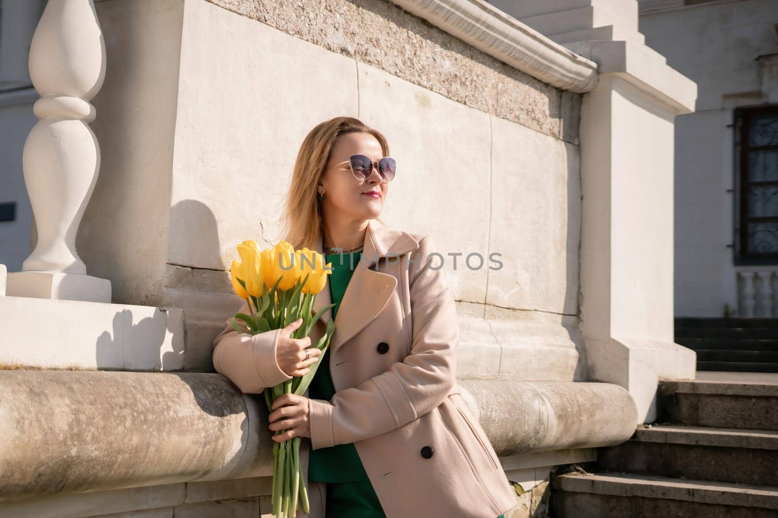 Woman holding yellow tulips, leaning against stone wall. Women's holiday concept, giving flowers