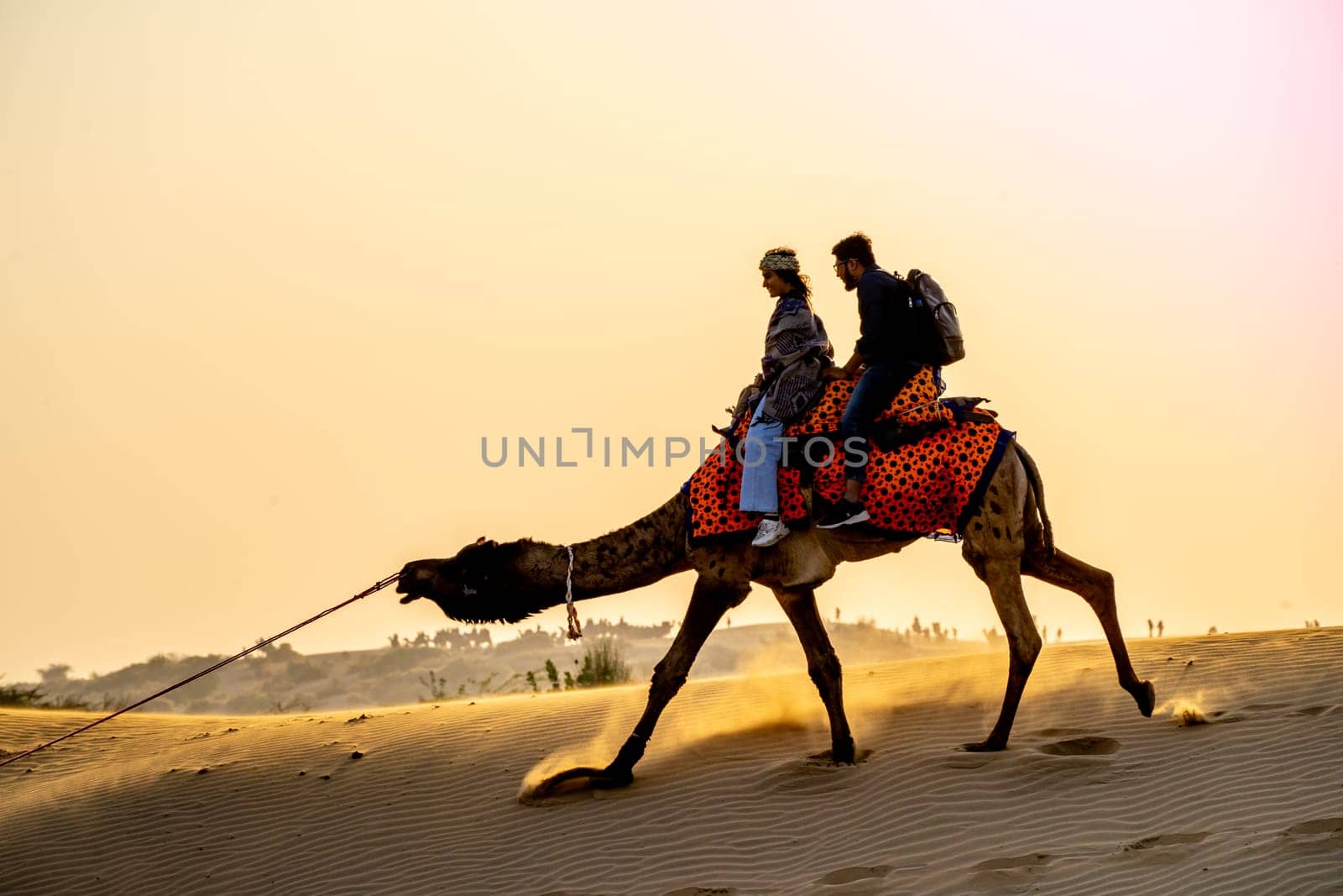 Jaisalmer, Rajasthan, India - 25th Dec 2023: Young couple tourists sitting on camel enjoying the walk sand dunes in sam or dubai