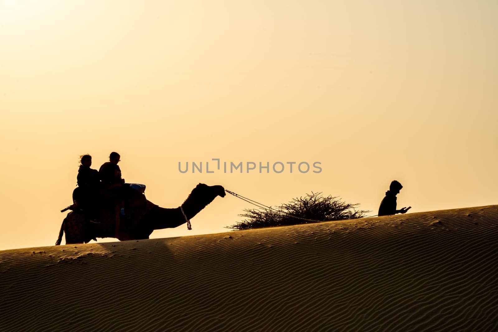 Silhouette of camel with two people sitting on it crossing over sand dunes in Sam Jaisalmer Rajasthan India