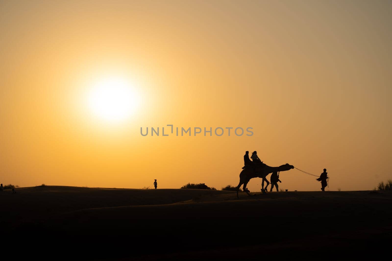 Silhouette of camel with two people sitting on it crossing over sand dunes in Sam Jaisalmer Rajasthan India