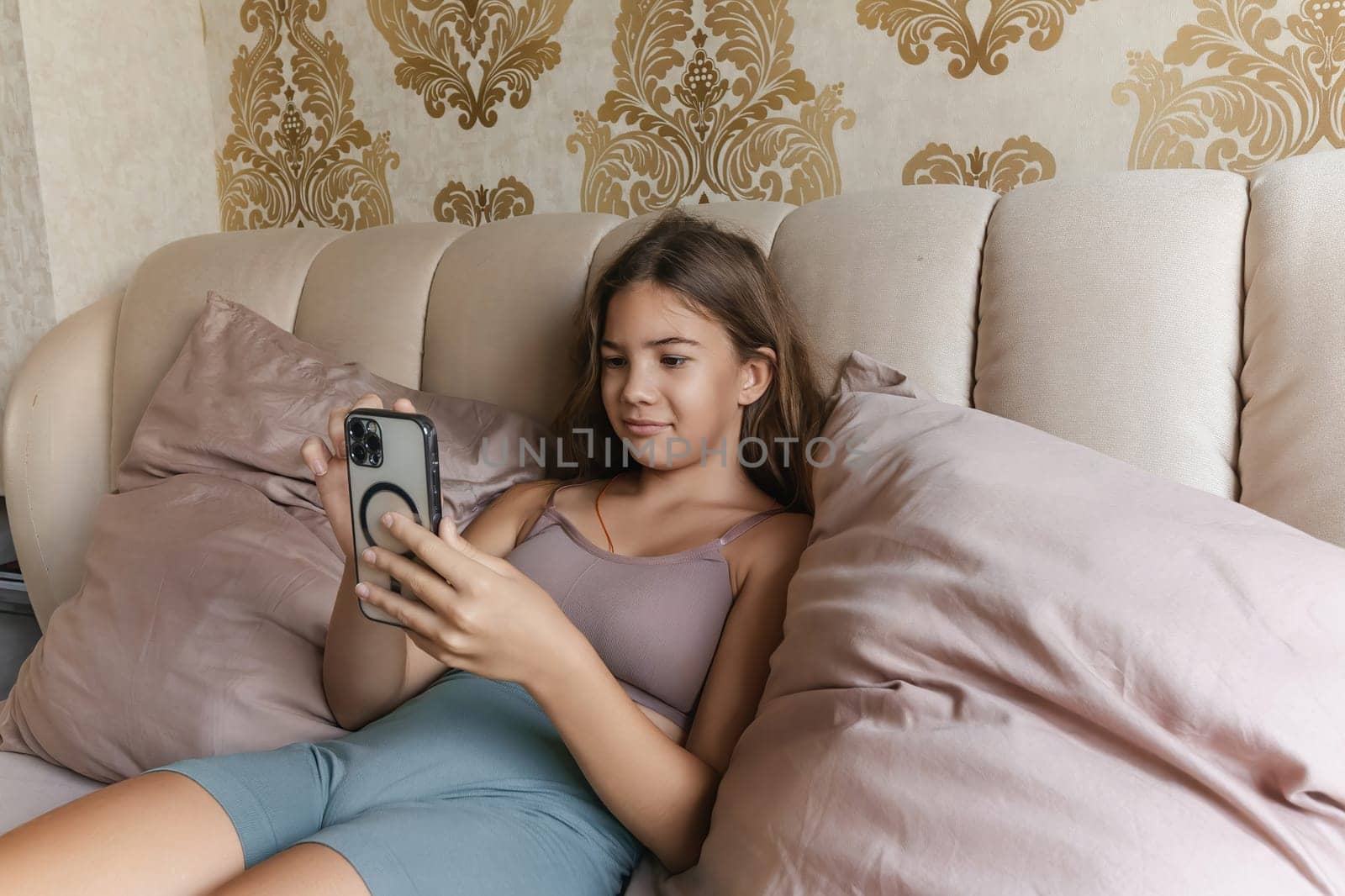 A girl is laying on a bed with a cell phone in her hand. She is smiling and she is enjoying herself