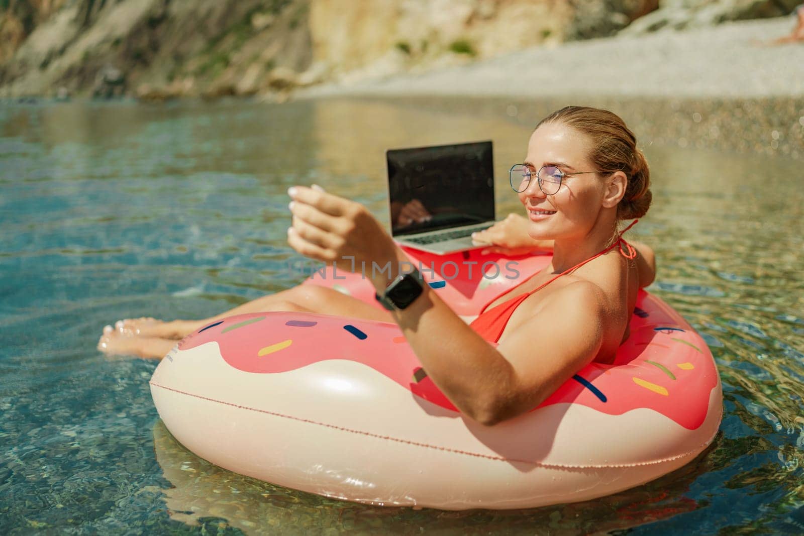 Woman laptop sea. Freelancer woman in sunglases floating on an inflatable big pink donut with a laptop in the sea. People summer vacation rest lifestyle concept