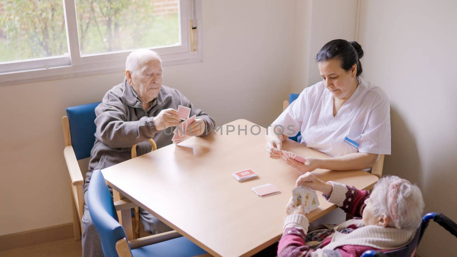 Senior people and caregiver playing cards in a nursing home by ivanmoreno
