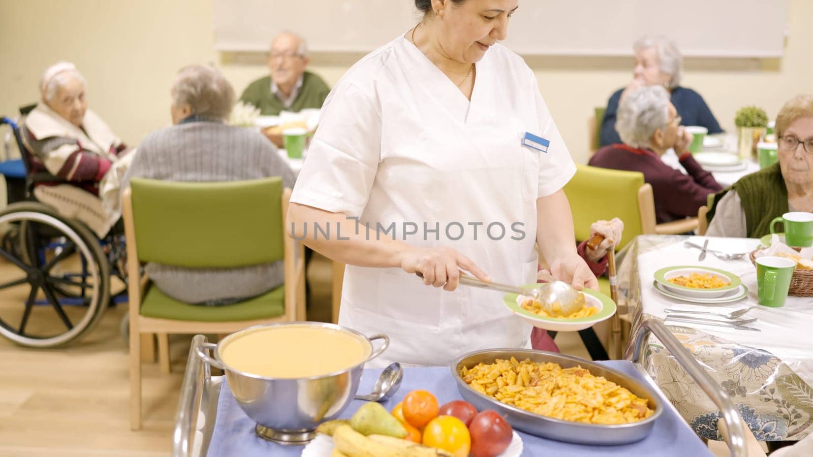 Cook serving pasta at seniors sitting in geriatric dinning room by ivanmoreno