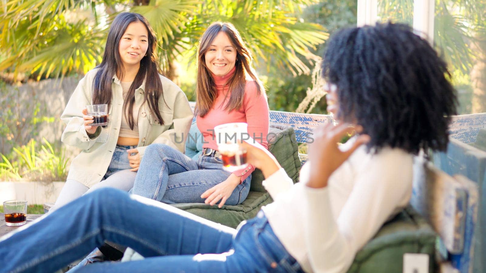 Woman arriving and sitting with a group of multi-ethnic fiends chilling on the garden drinking wine during sunset