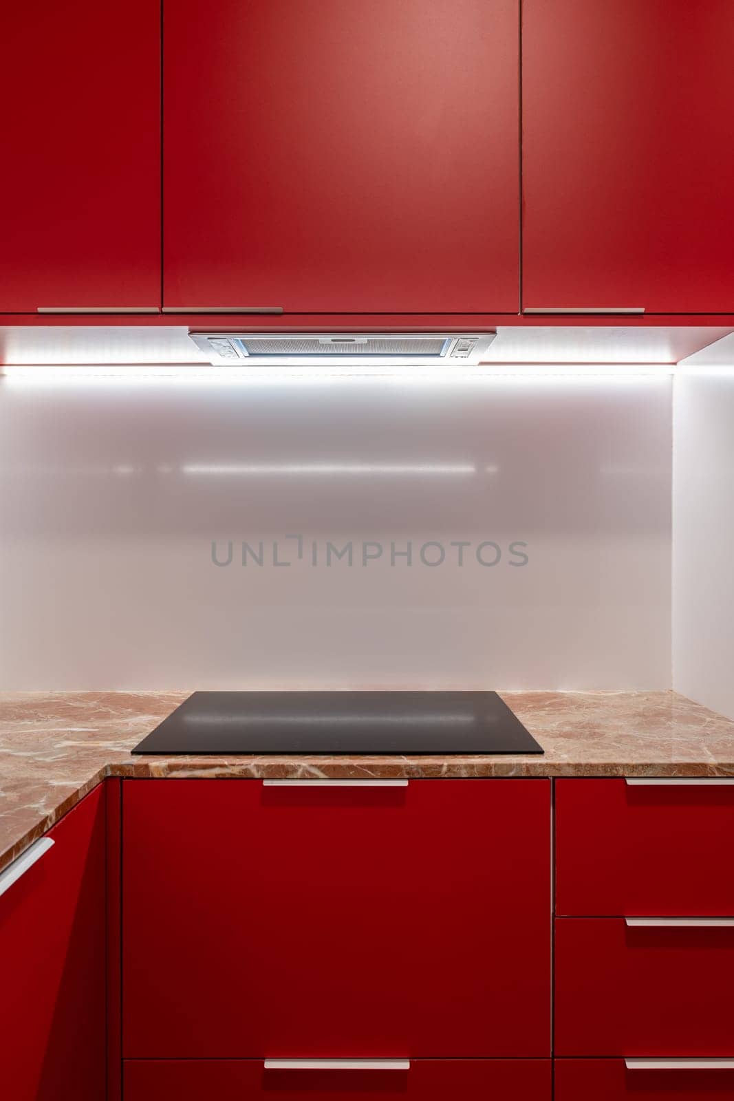A contemporary kitchen featuring a bold red cabinet with a marble countertop and modern lighting