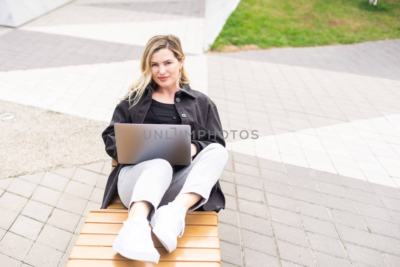 Young woman sitting on online meeting in outdoor cafe, talking to laptop camera, explaining something, drinking coffee. High quality photo