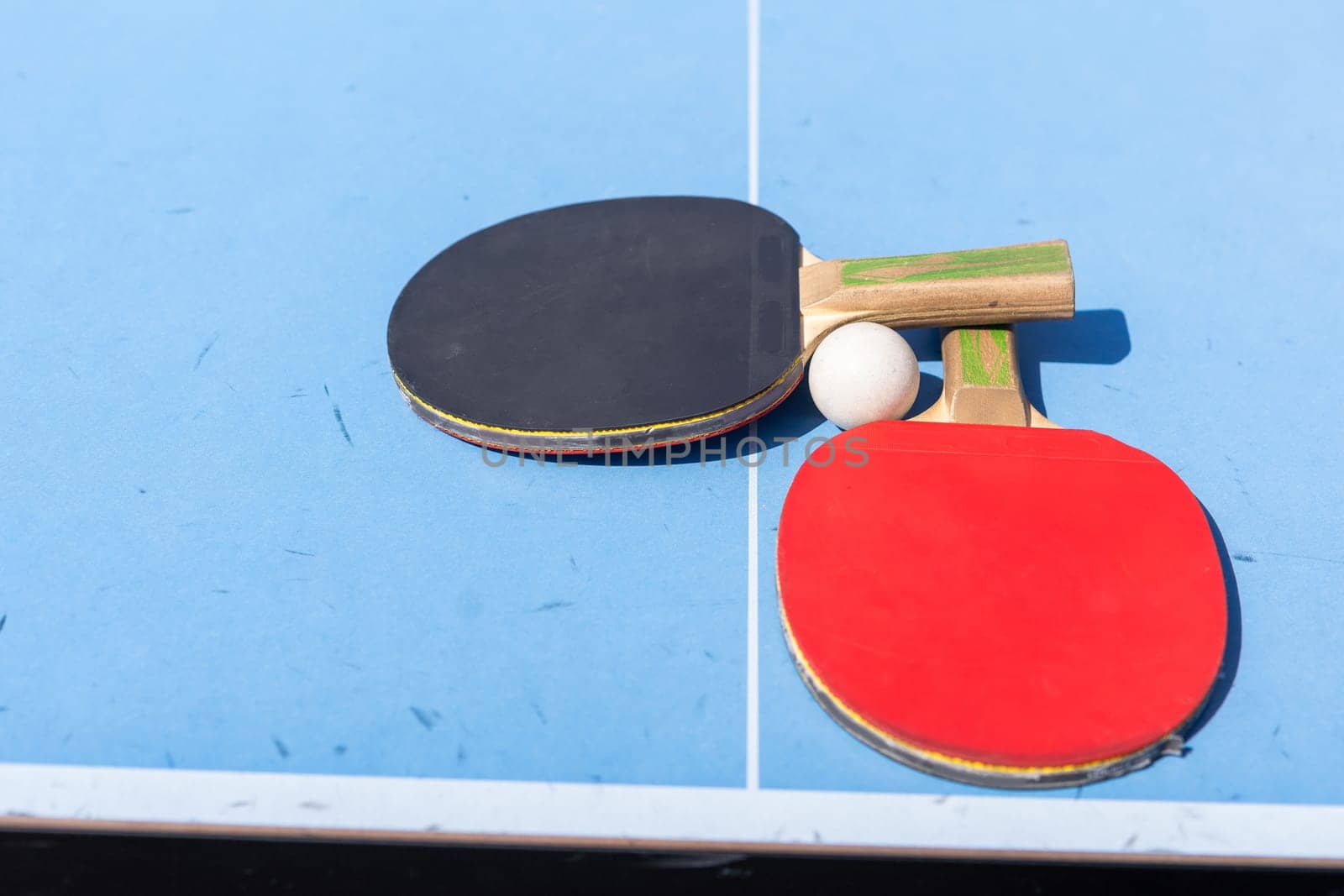 Red and black Table Tennis Paddles and ball on the blue table tennis table with net. Ping Pong concept with copy space. High quality photo