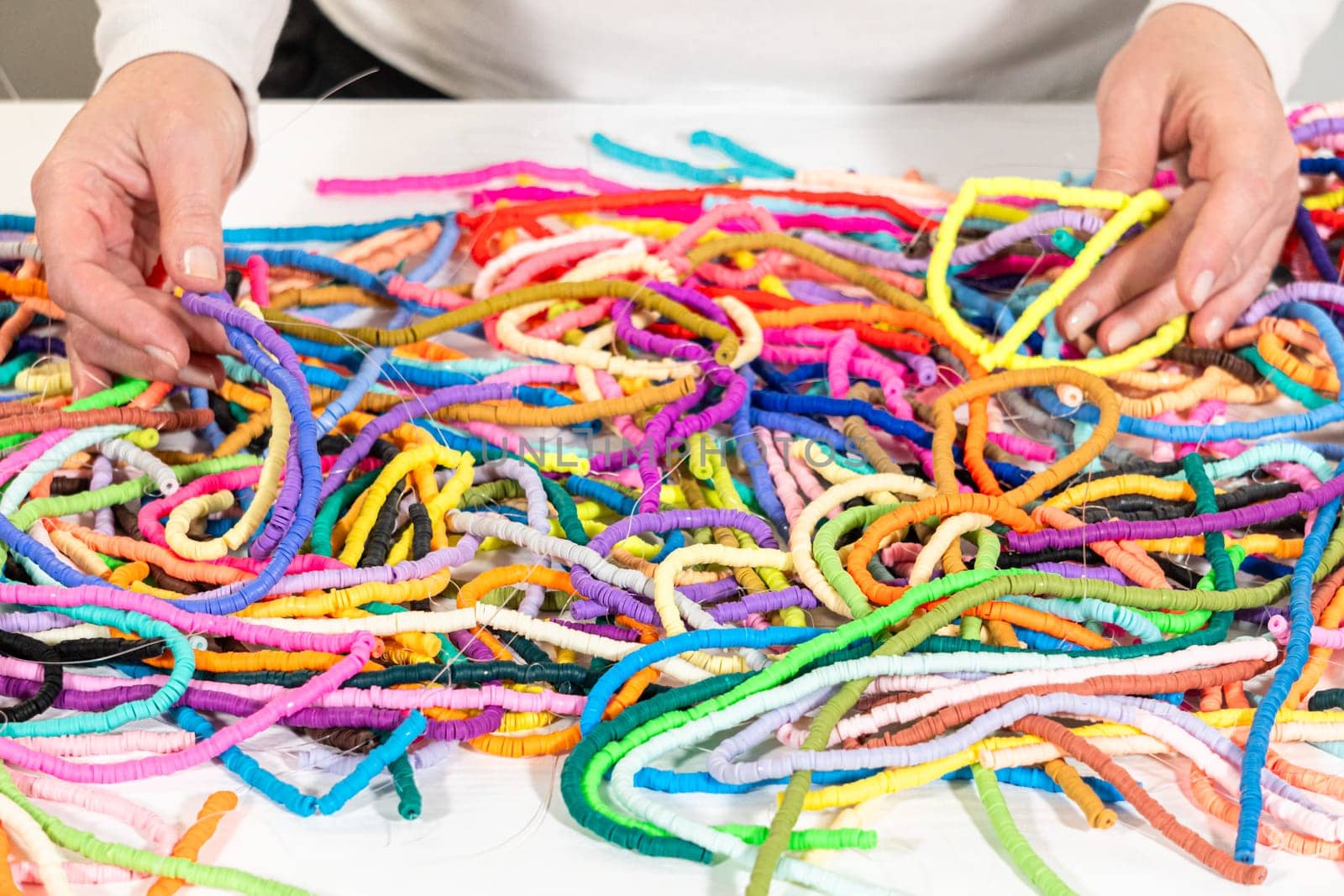 A vibrant collection of clay beads, neatly arranged by color on a white table, ready to inspire young crafters to create their own unique bracelets.