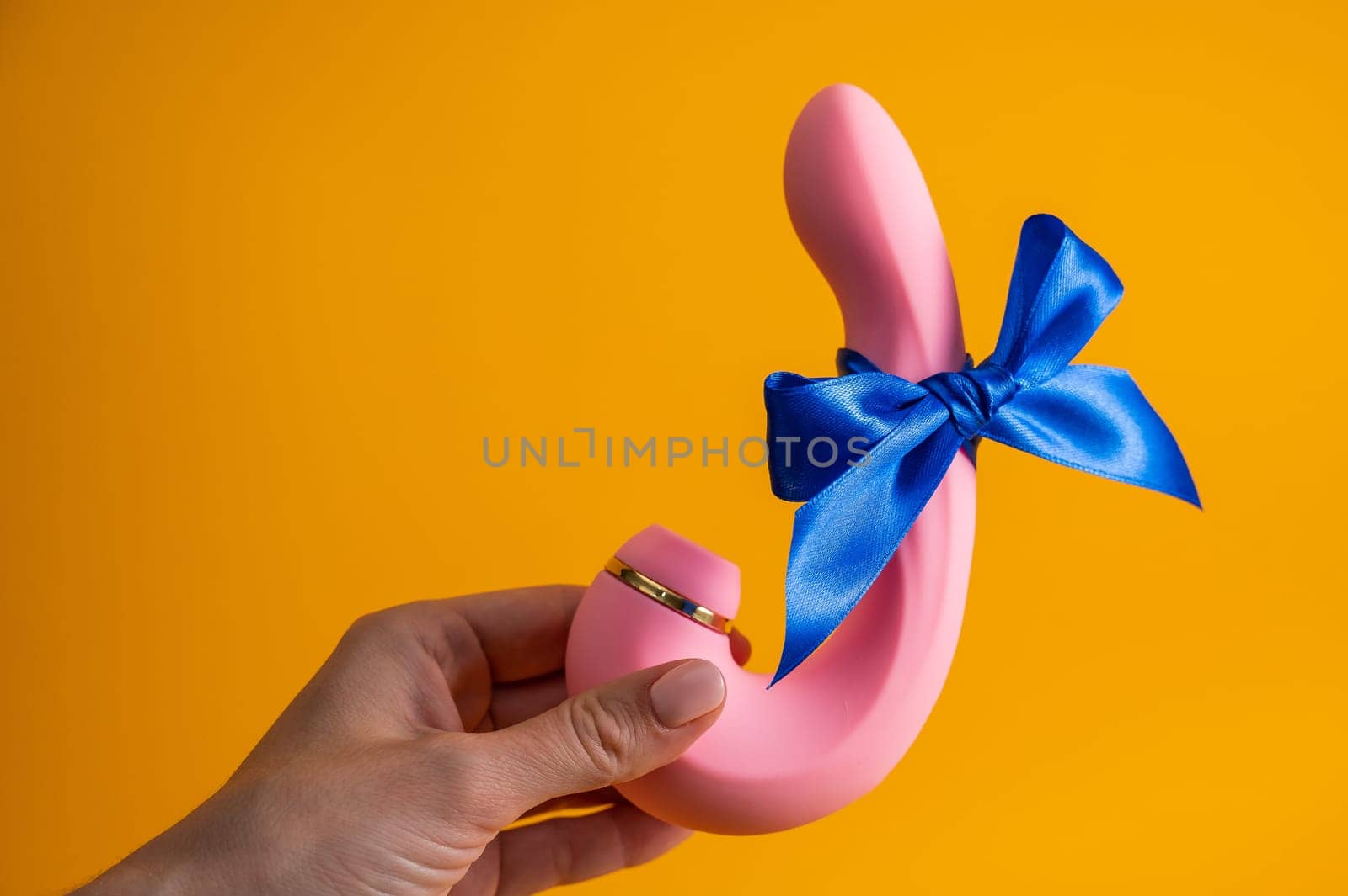 Woman holding curved pink vibrator with blue ribbon on orange background