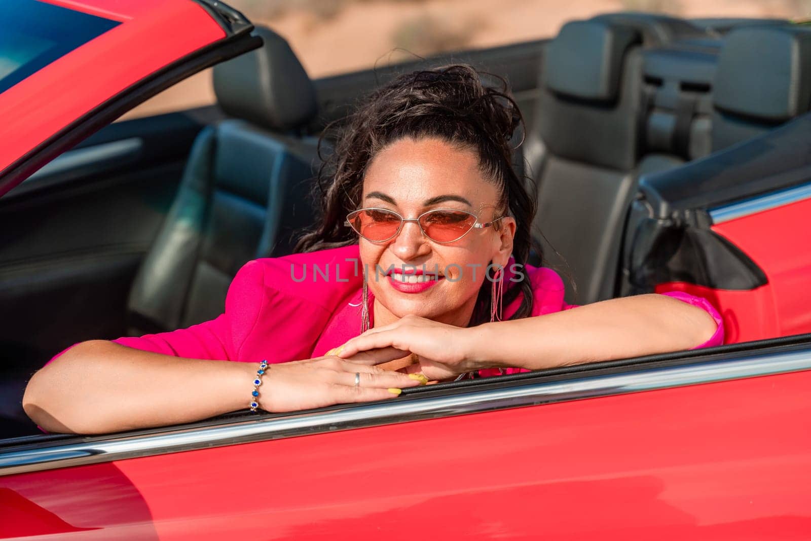 A woman in a pink jacket is sitting in a red convertible. She is wearing sunglasses and has her hand on her hip. Scene is relaxed and carefree. by Matiunina
