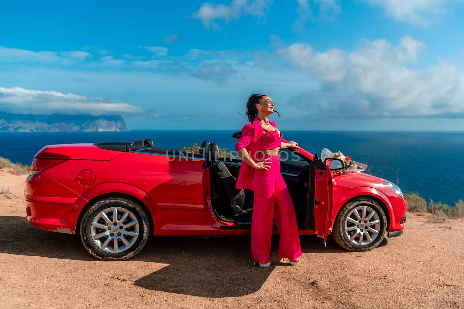 A woman stands in front of a red convertible car, holding a bouquet of flowers. Concept of freedom and adventure, as the woman is dressed in a red outfit and poses in front of the car