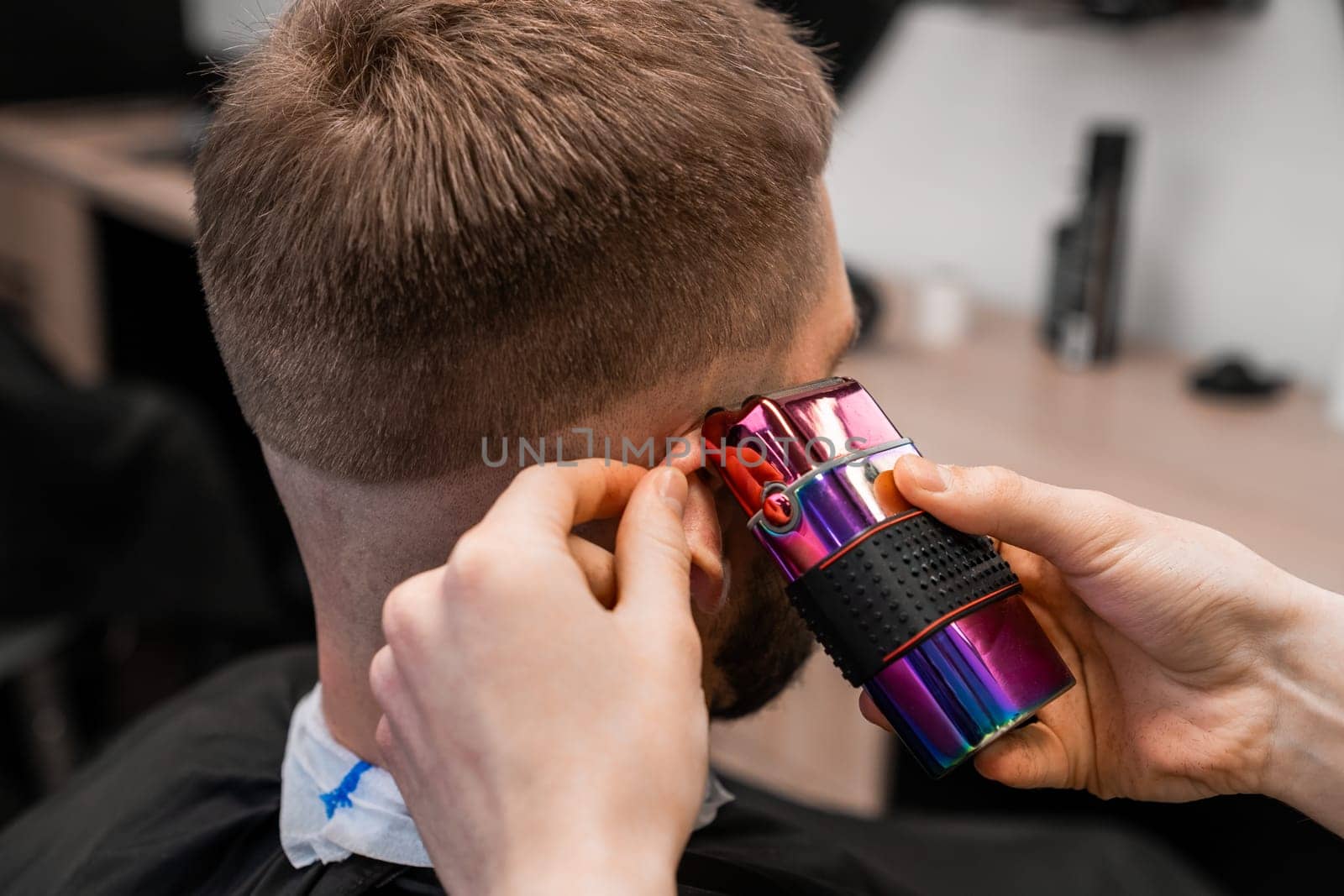 Barber uses shaver machine to cut young man hair in barbershop closeup. Master does modern haircut to male client in professional salon