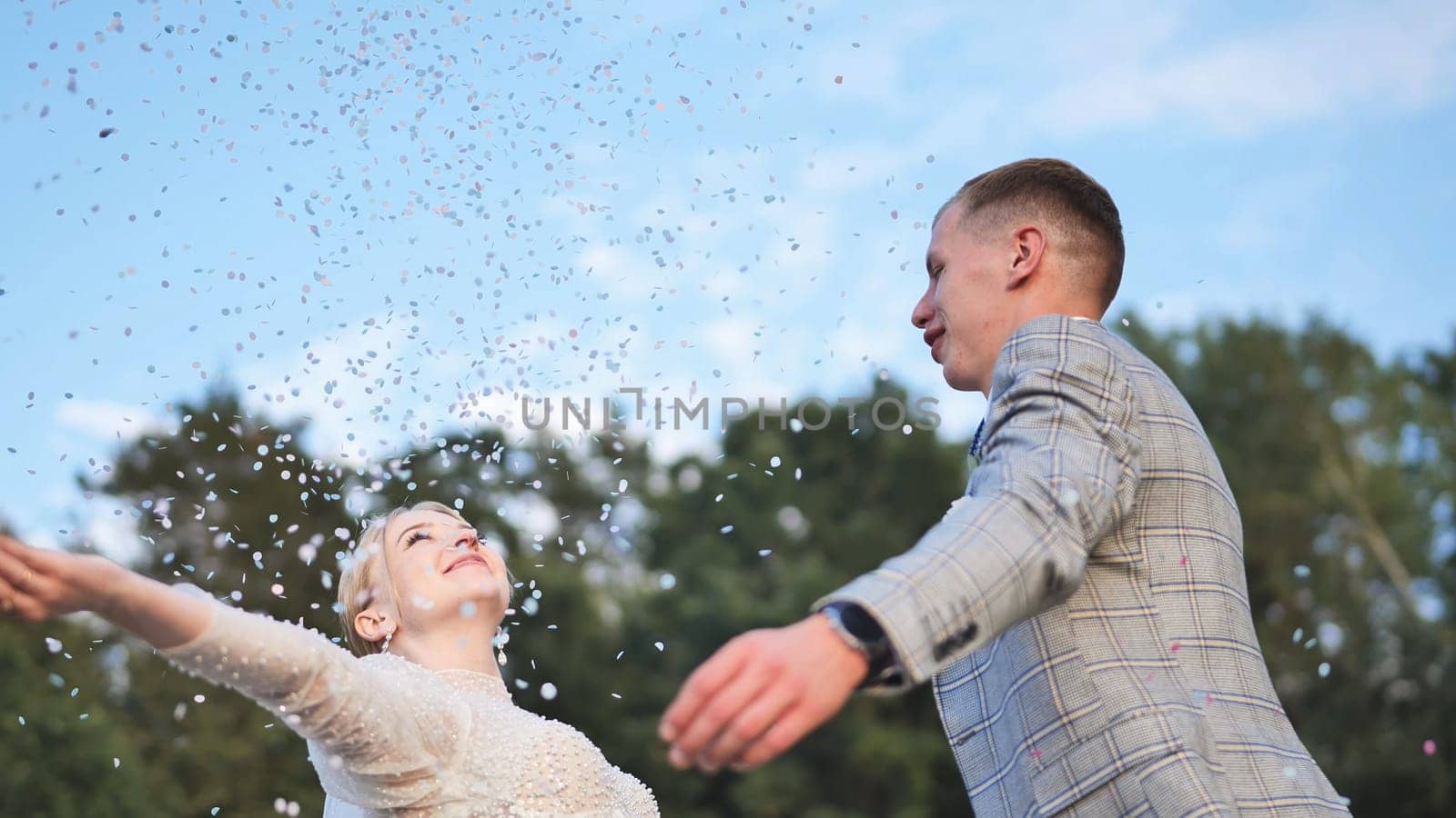 The bride and groom toss confetti above them and embrace
