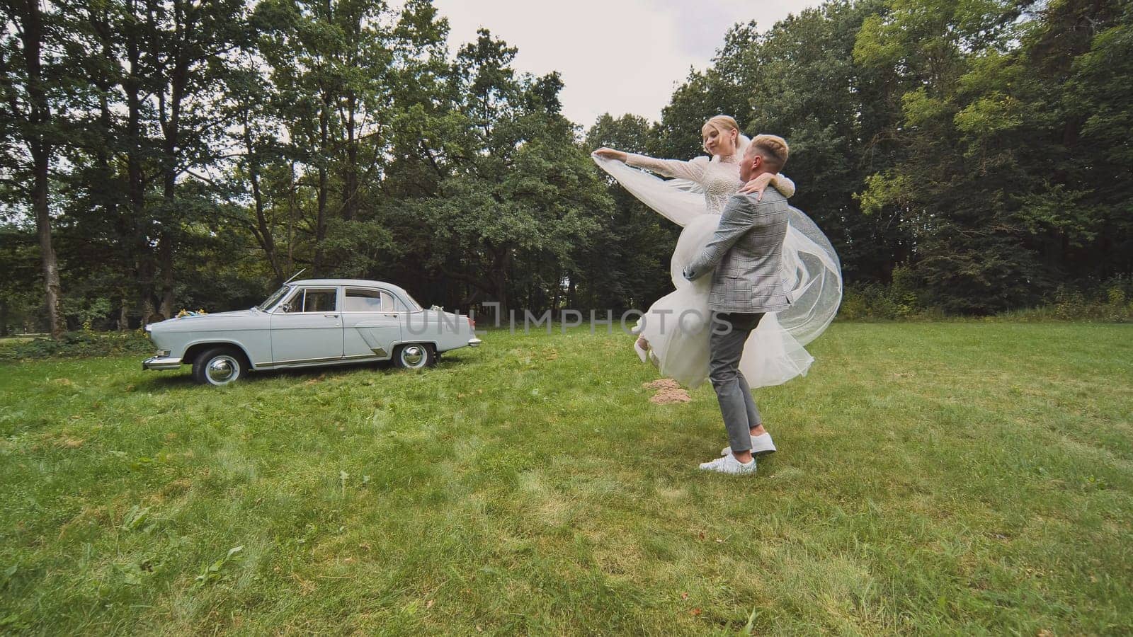 Bride and groom twirling in the background of a retro automobile. by DovidPro