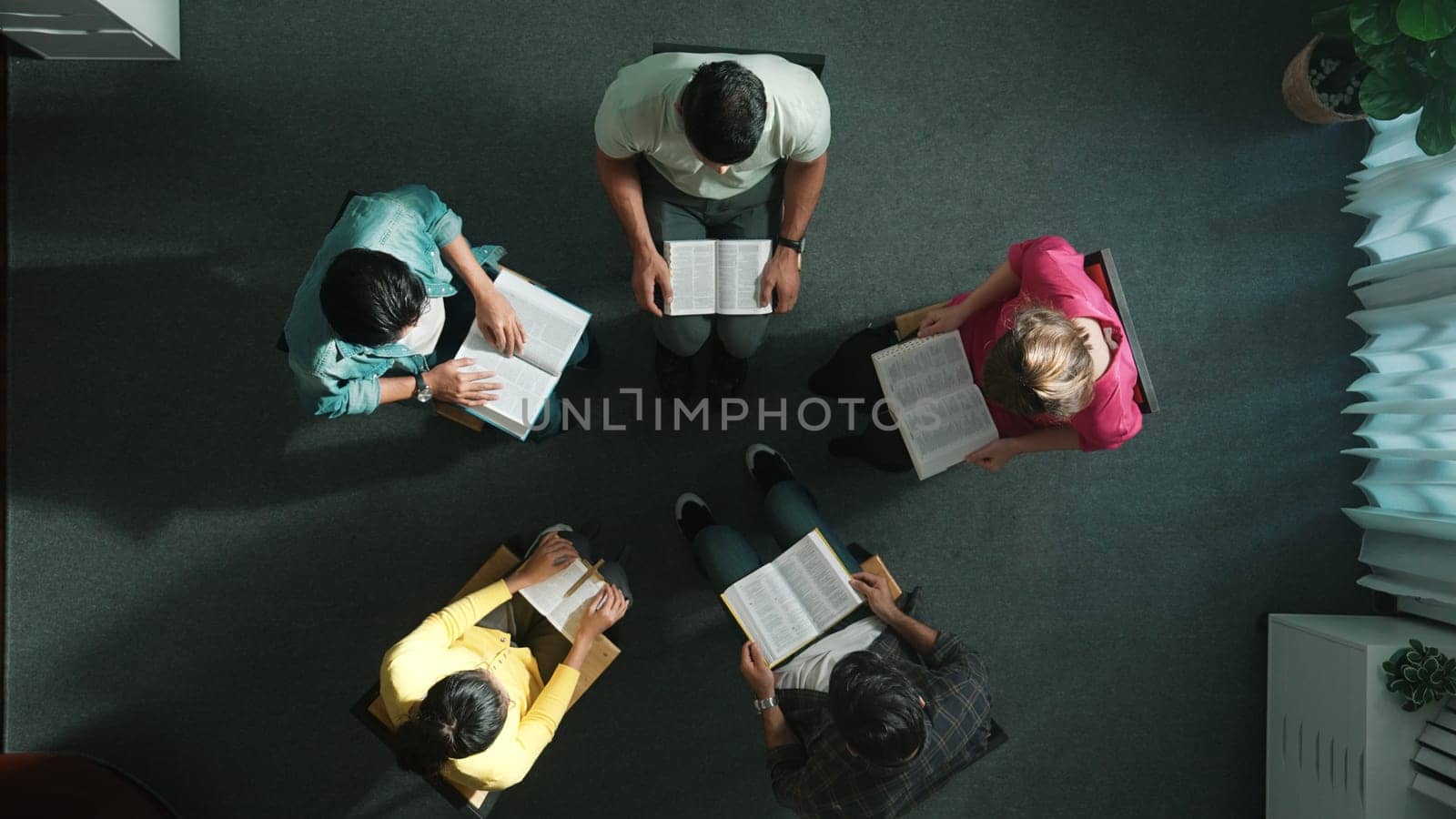 Top down view of prayer reading at bible book and sitting in circle with bible book on laps. Aerial view of diverse people looking at book while studying with faith, trust and hope, calm. Symposium.