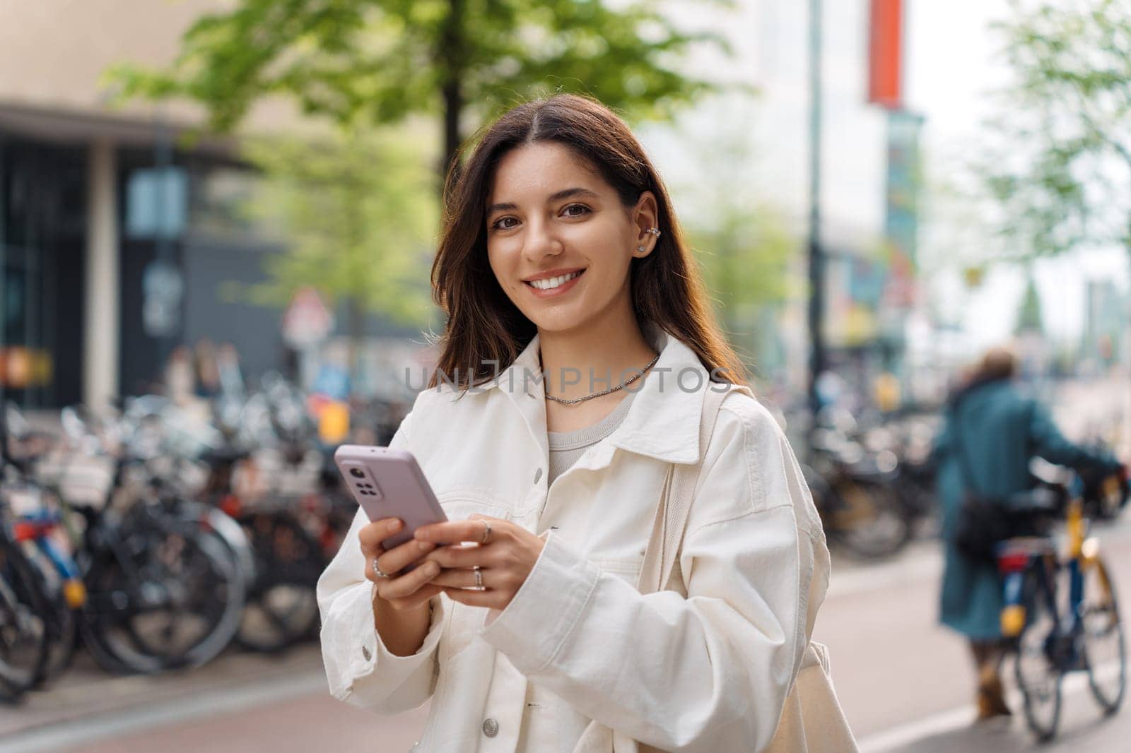 Mixed-race LGBT proud and confident Turkish young woman holding a phone in the street smiling wearing white casual clothes.