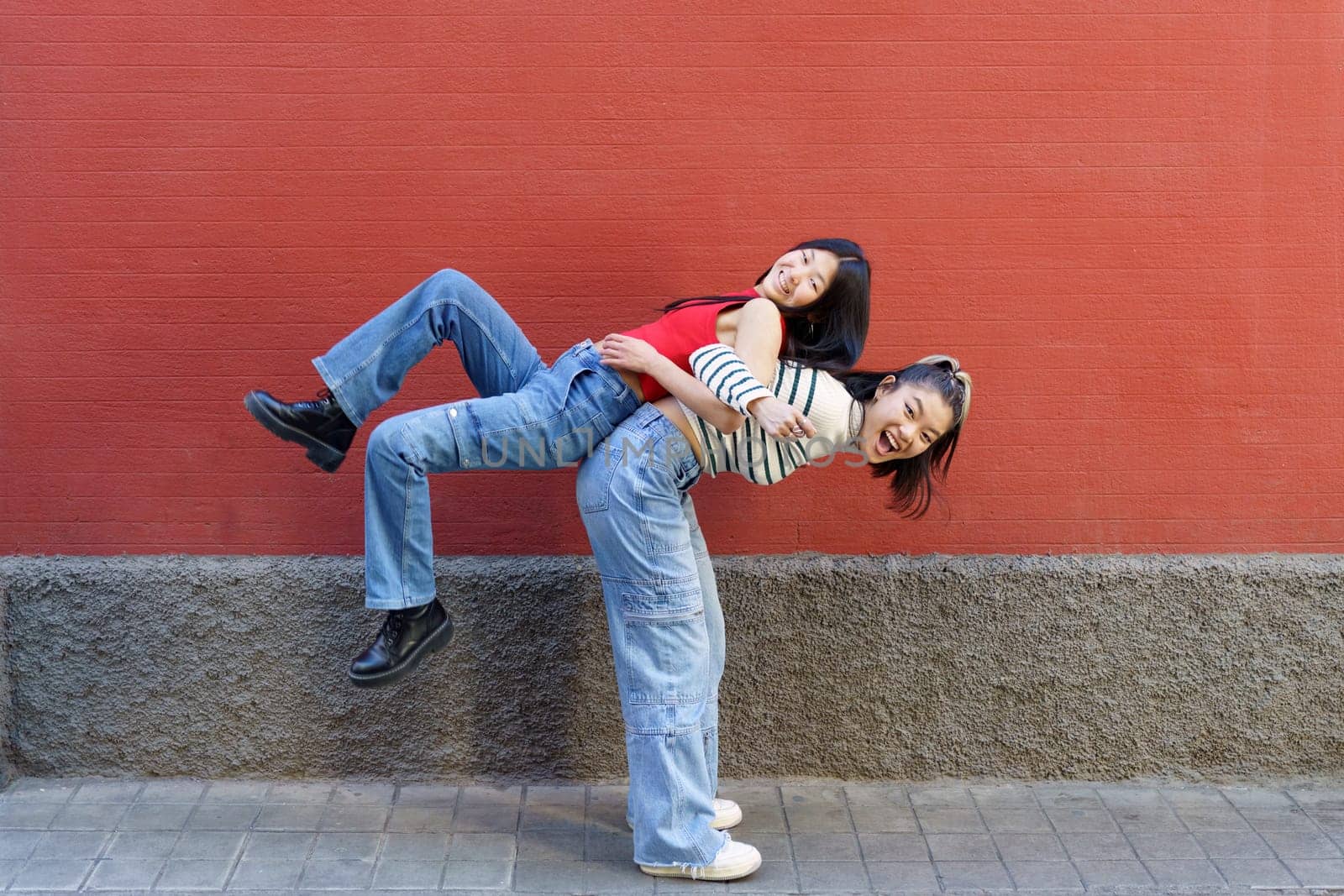 Happy Asian woman lifting friend on back by javiindy