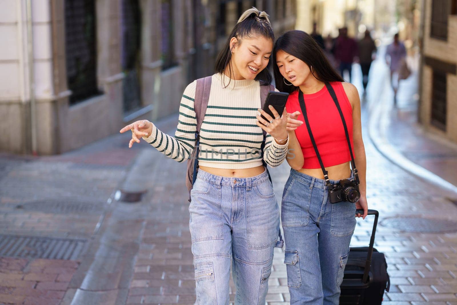 Asian girlfriends traveling together walking on street and browsing smartphone by javiindy