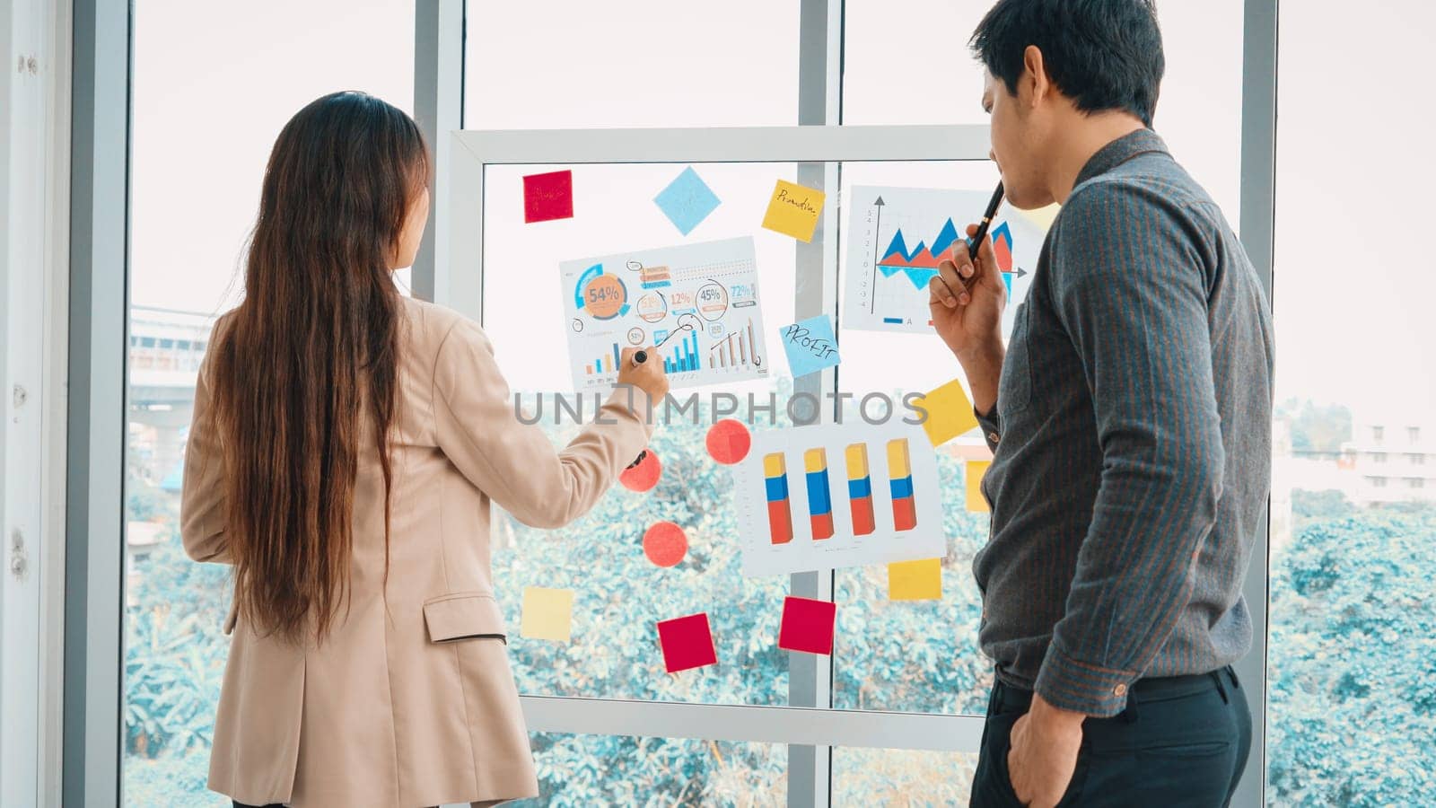 Business people work on project planning board in office and having conversation with coworker friend to analyze project development . They use sticky notes posted on glass to make it organized. Jivy