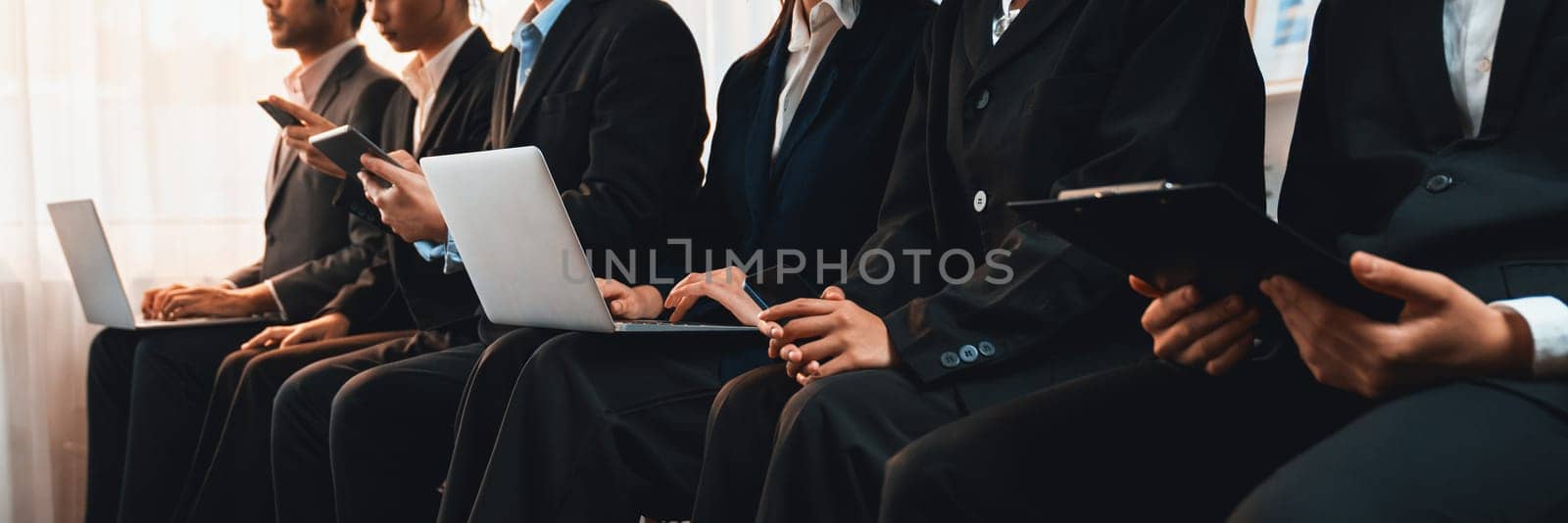 Asian job applicant in identical formal wear sitting in waiting room for job interview. Office worker or business people working in cramped room together using laptop and phone. Trailblazing