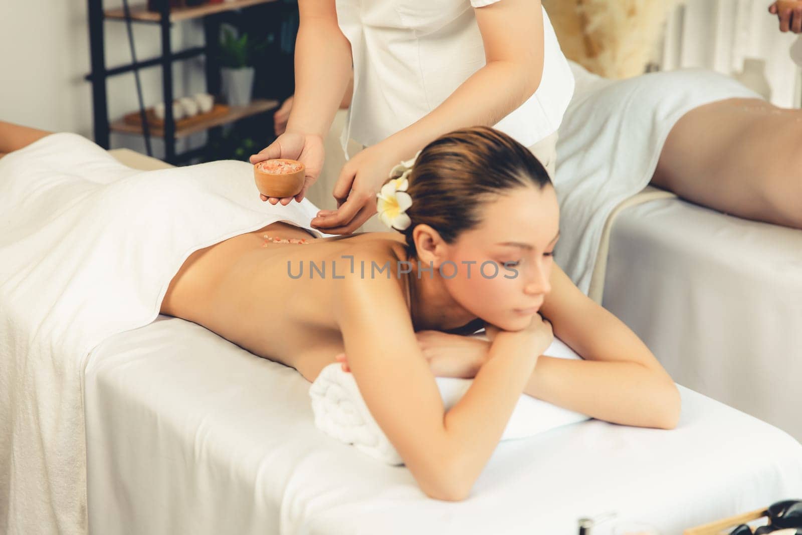 Blissful couple customer having exfoliation treatment in luxury spa salon with warmth candle light ambient. Salt scrub beauty treatment in health spa body scrub. Quiescent