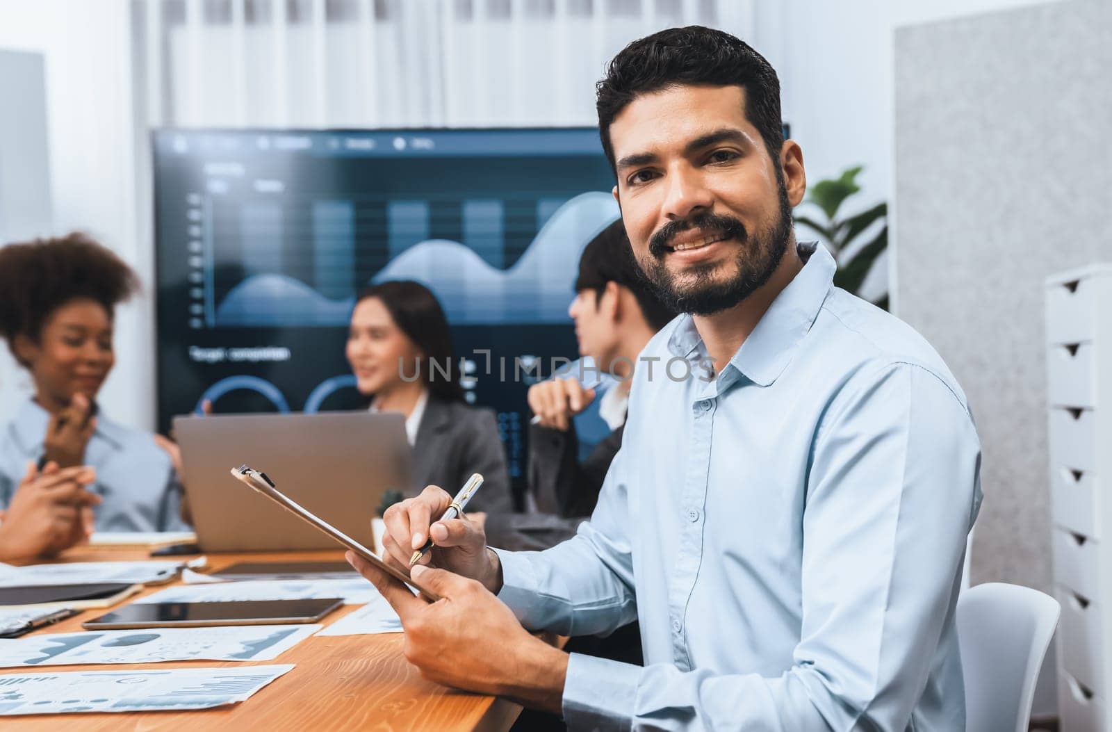 Portrait of happy and smiling businessman with group of coworkers on meeting with screen display business dashboard in background. Confident office worker at team meeting. Concord