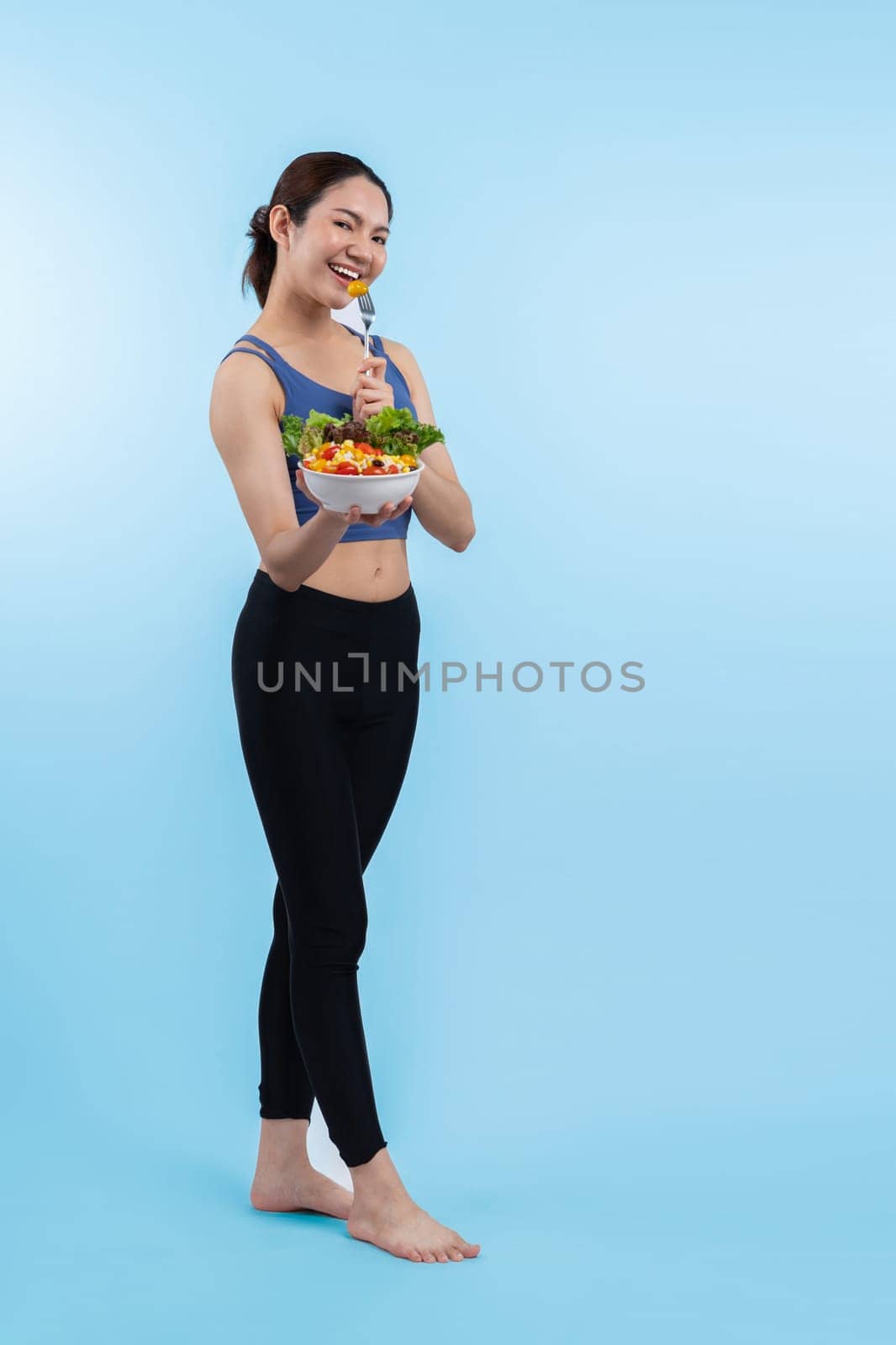 Young sporty Asian woman in sportswear holding salad bowl fill with vibrant of fruit and vegetable. Natural youthful and fit body lifestyle with balance nutrition on isolated background. Vigorous