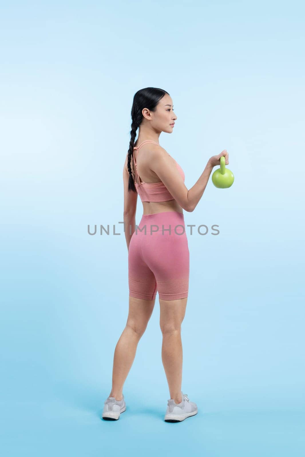 Vigorous energetic woman doing kettlebell weight lifting exercise on isolated background. Young athletic asian woman strength and endurance training session as body workout routine.