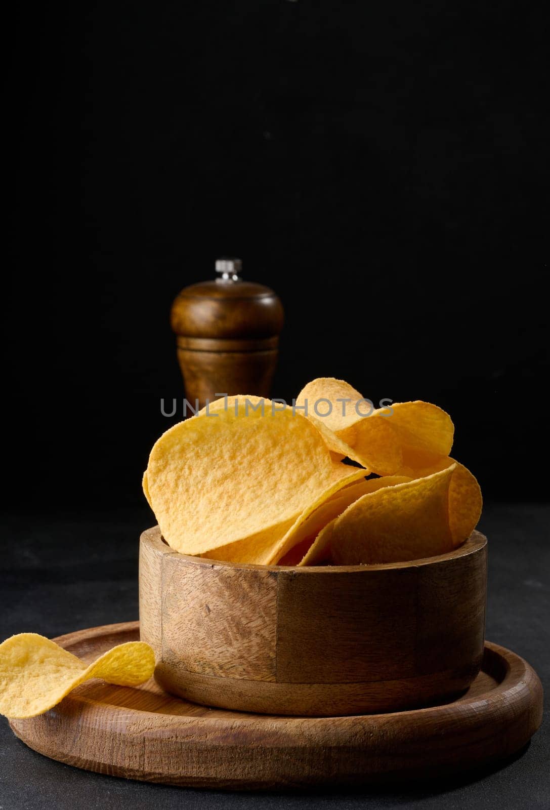 Potato chips in a wooden bowl on a black table, snack by ndanko