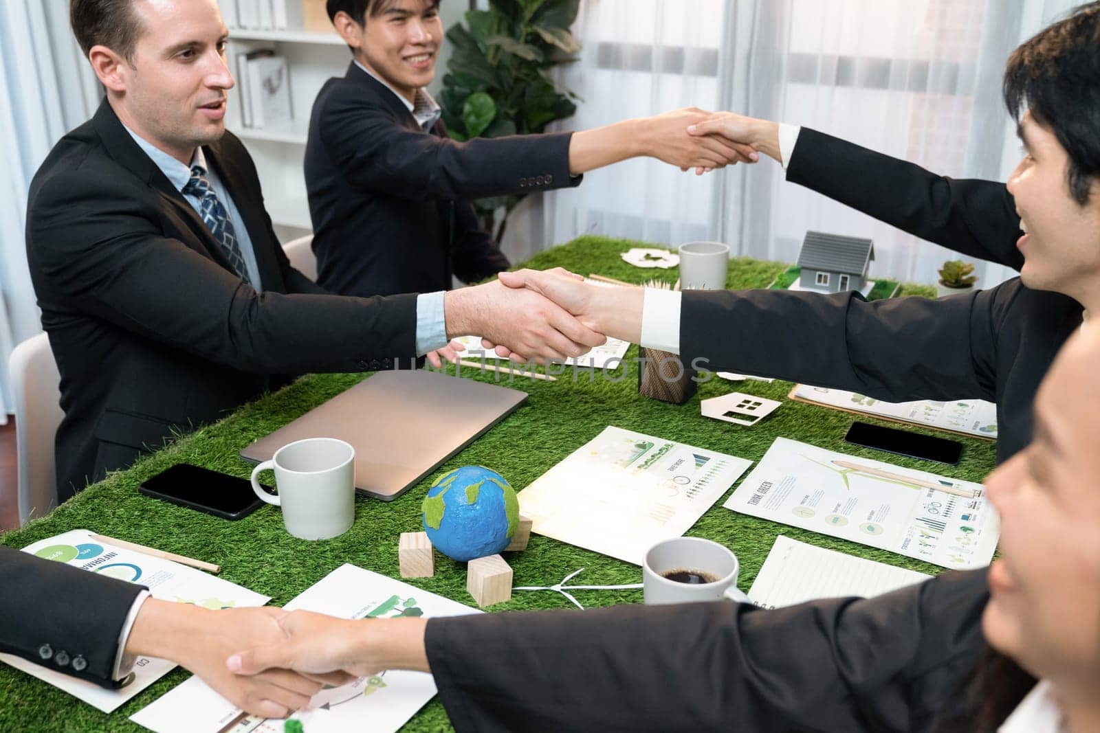 Handshaking between green business partnership over meeting table. Quaint by biancoblue