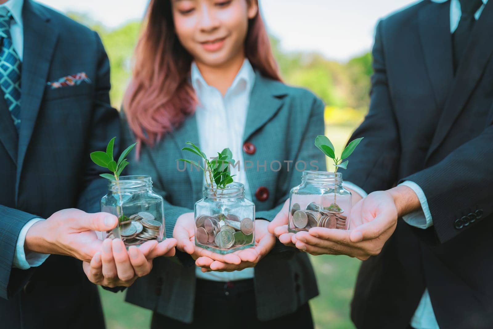 Concept of sustainable money growth investment with glass jar filled with money savings coins with businesspeople as eco-friendly financial investment nurtured with nature and healthy retirement. Gyre