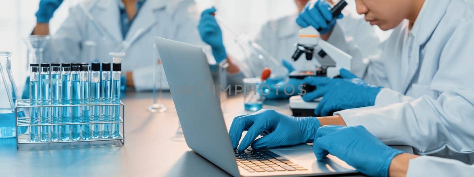 Dedicated group of scientist conduct chemical experiments and research in medical lab as groundbreaking developing for new vaccine drug or antibiotic and studying test result on laptop. Neoteric