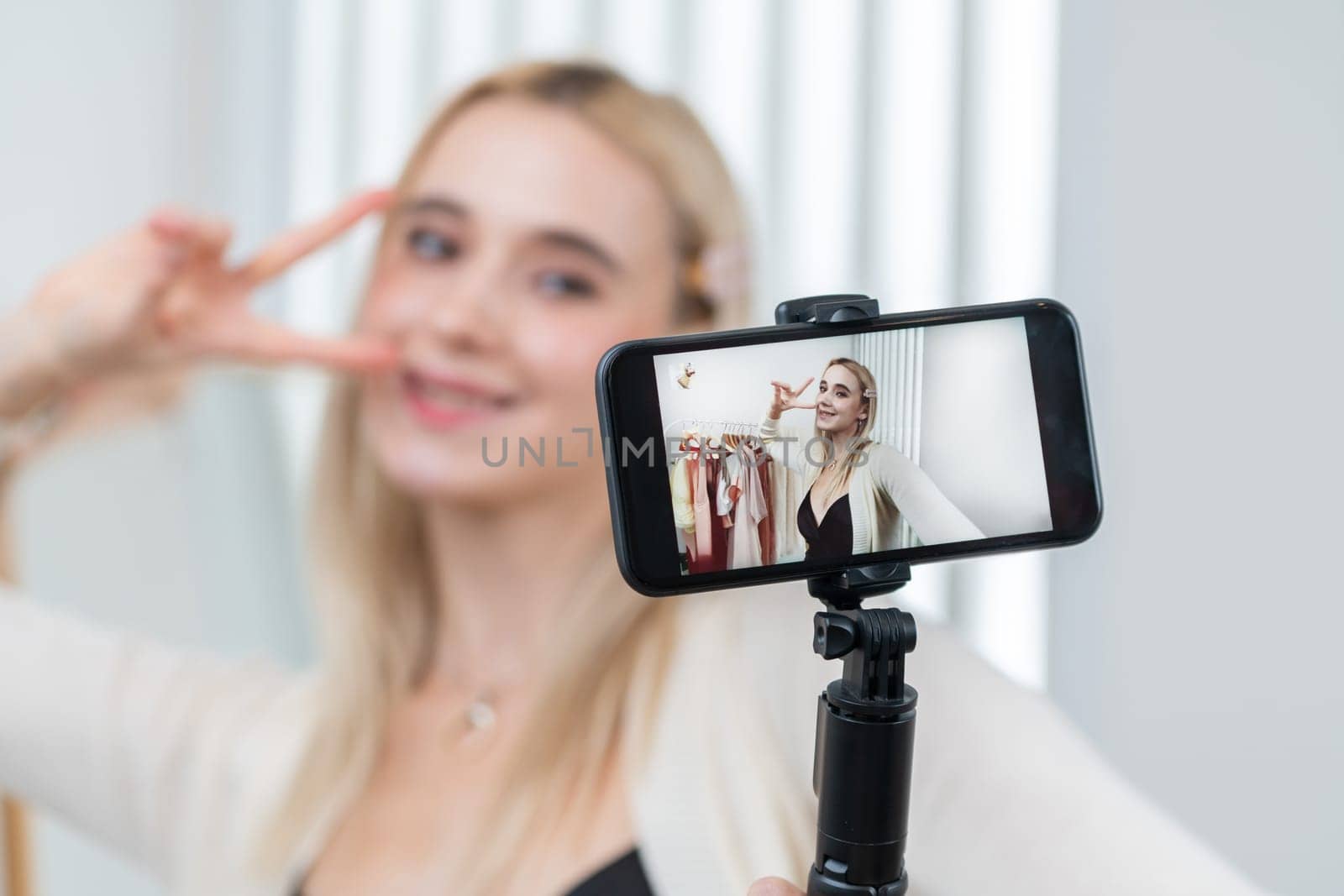 Young social medial content creator woman make fashion video. Blogger smiles and using phone stick selfie while making persuasive online clothing sell vlog to audience or follower. Blithe