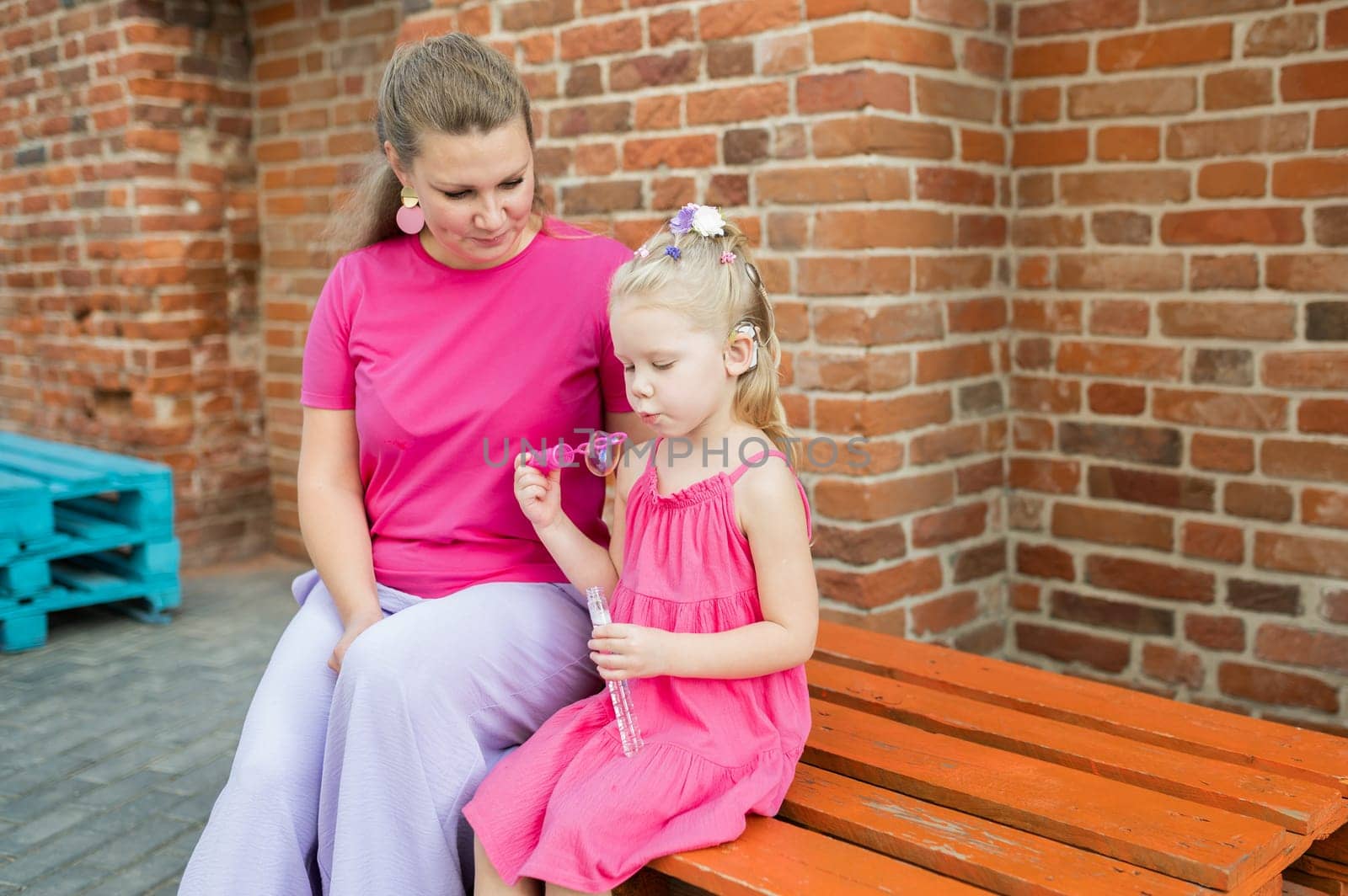 Blonde little girl with cochlear implant playing with her mother outdoor. Hear impairment deaf and health concept. Disability and inclusion. Copy space by Satura86