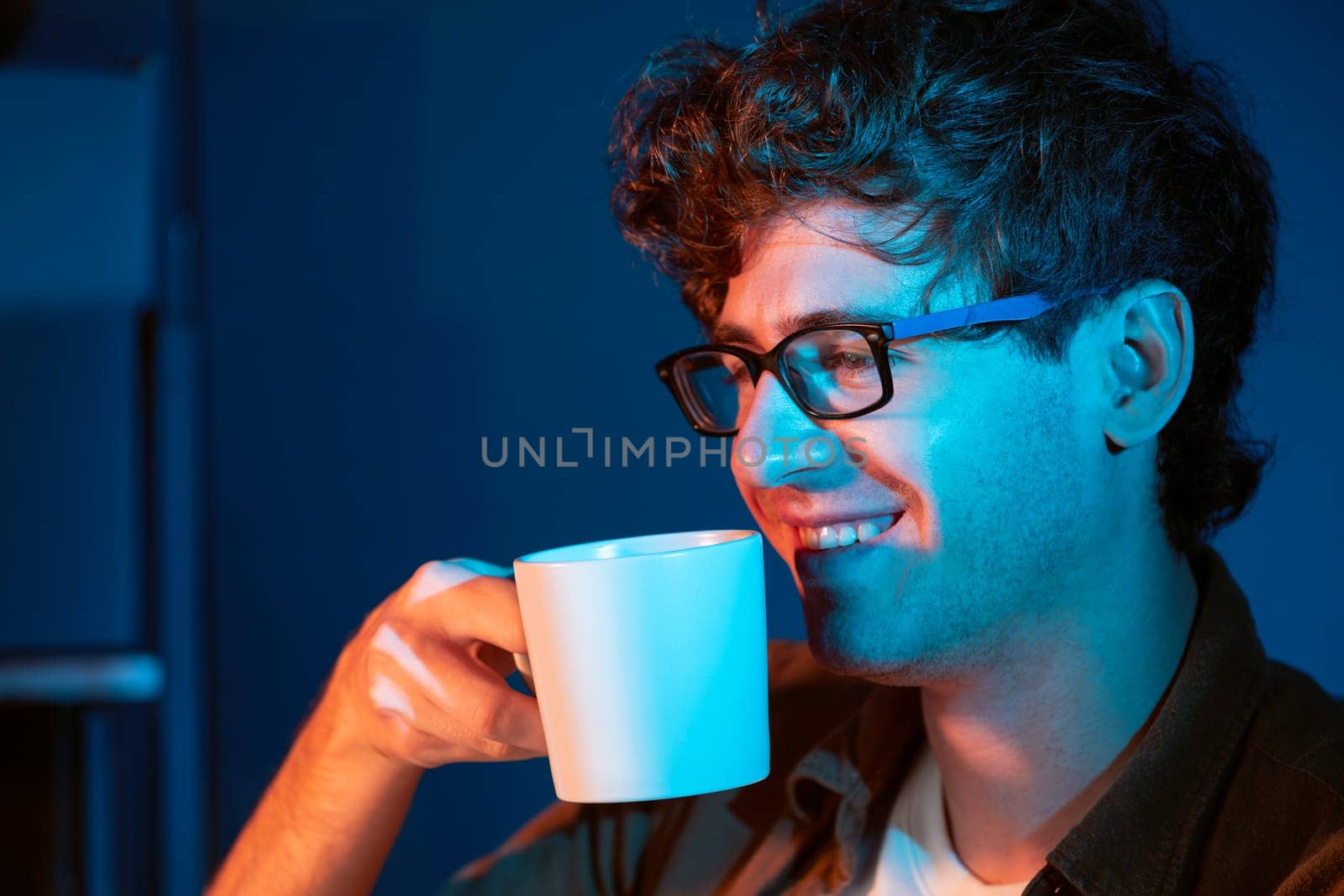 Young businessman working creative startup project job, drinking hot drink with coffee or tea while focusing on pc at neon light modern office with portrait view. Thinking marketing plan of. Gusher.