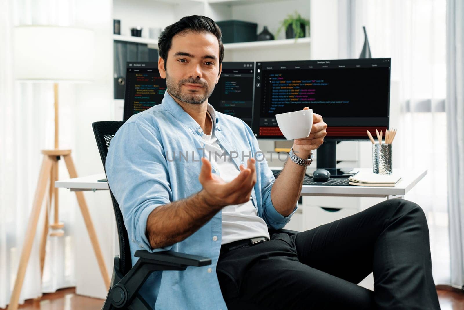 Profile's smart IT developer looking camera to pose holding coffee cup against on software development coding on two pc screen, presenting program update online website data at modern office. Surmise.