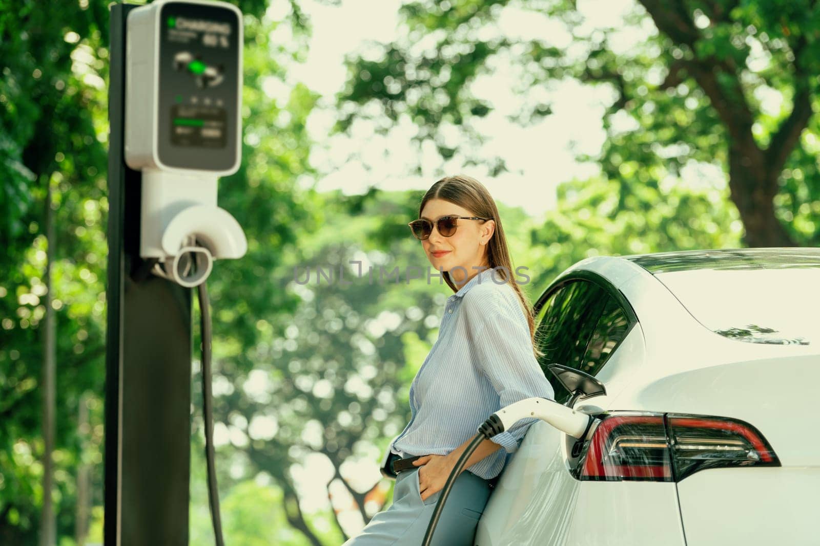 Young woman recharging battery for electric car during road trip. Exalt by biancoblue