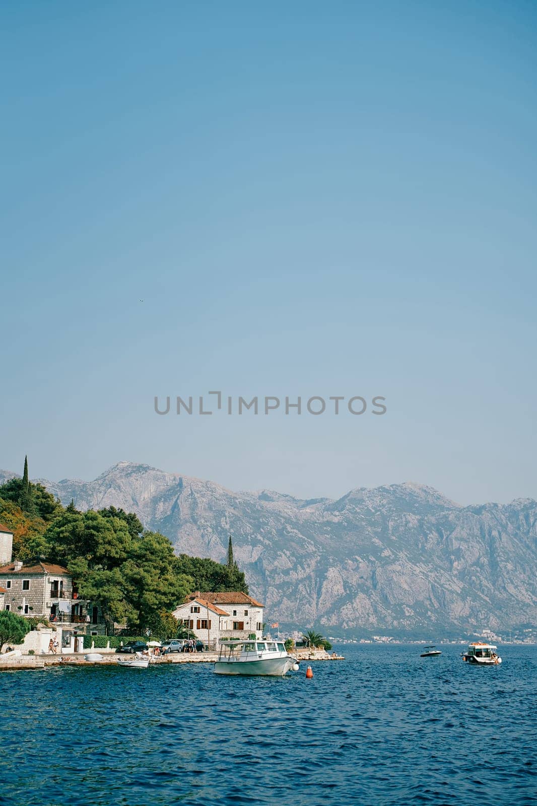 Boats stand off the coast of Perast with old houses among green trees. Montenegro by Nadtochiy