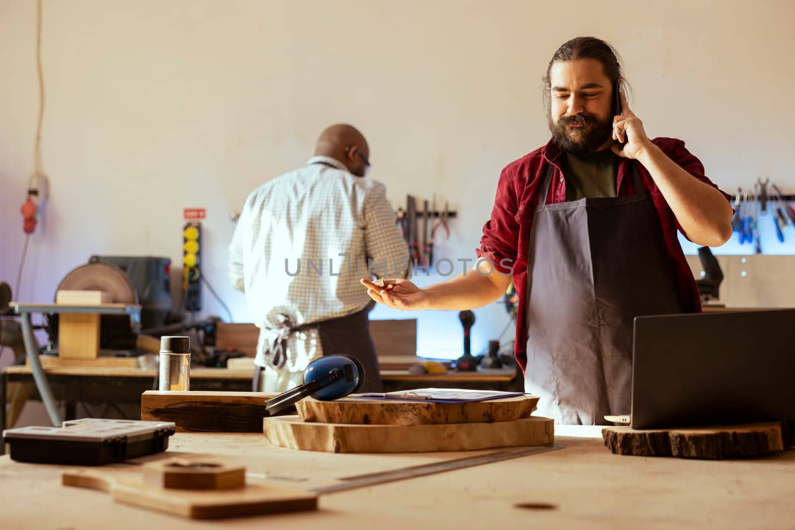 Cheerful carpenter in assembly shop talking on mobile phone with customer by DCStudio