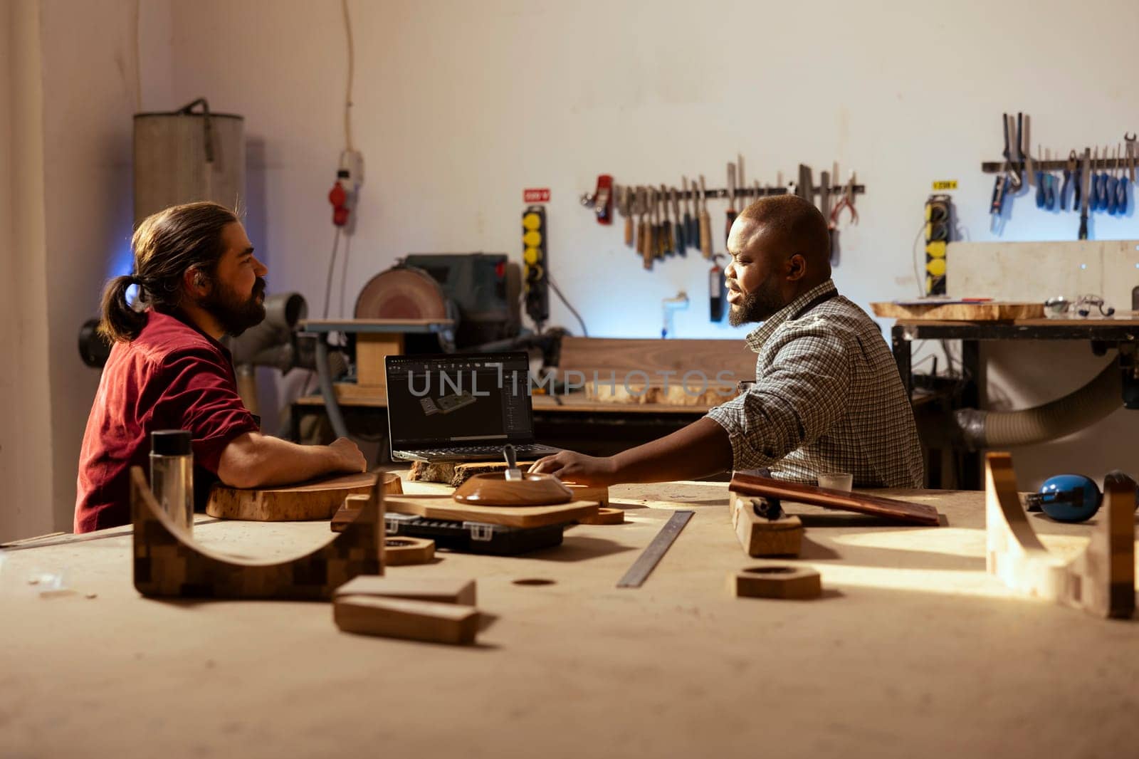 Woodworker and coworker using CAD software on laptop by DCStudio